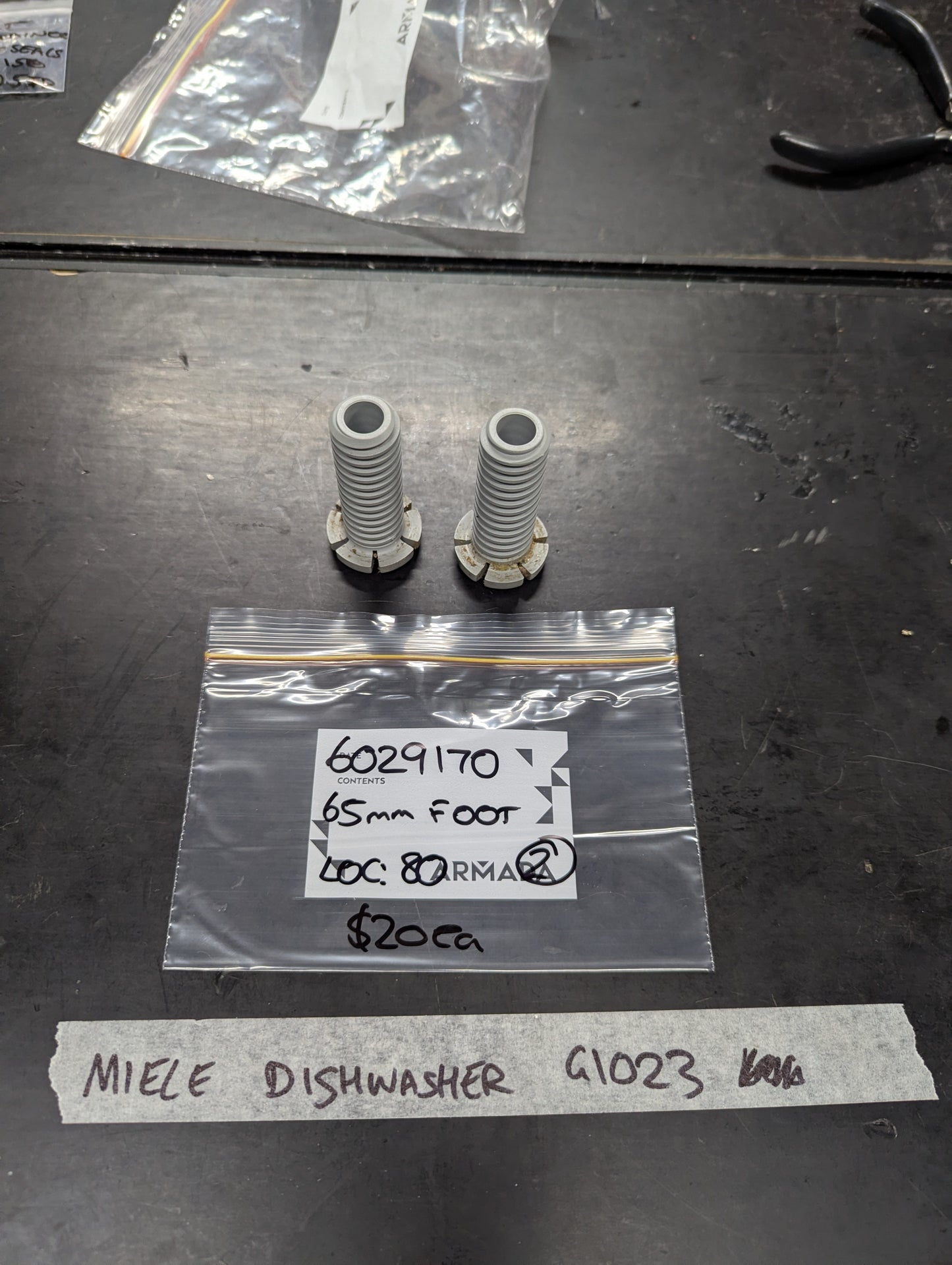 Pair of Miele dishwasher 65mm feet and labeled packaging displayed on a workbench