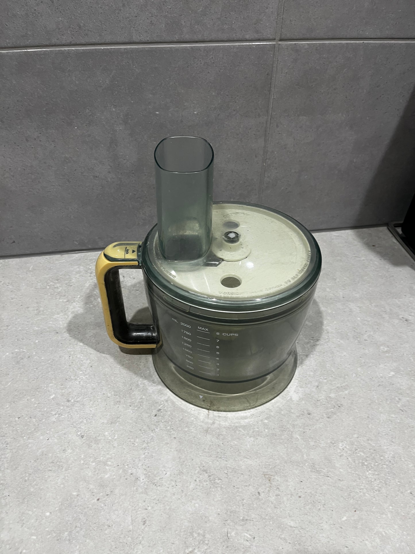 Food processor bowl with translucent dark plastic and yellow-black handle on countertop
