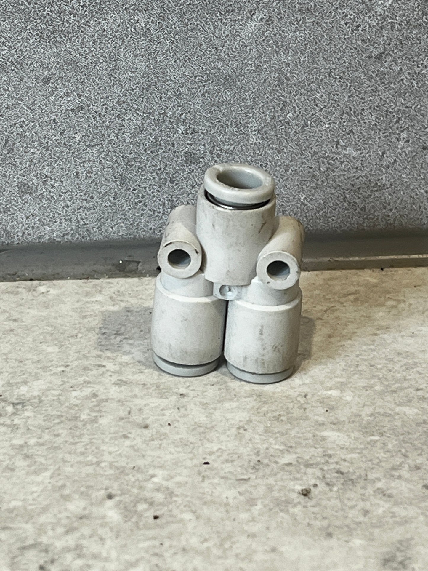 Push-to-connect pneumatic tee fitting on gray surface