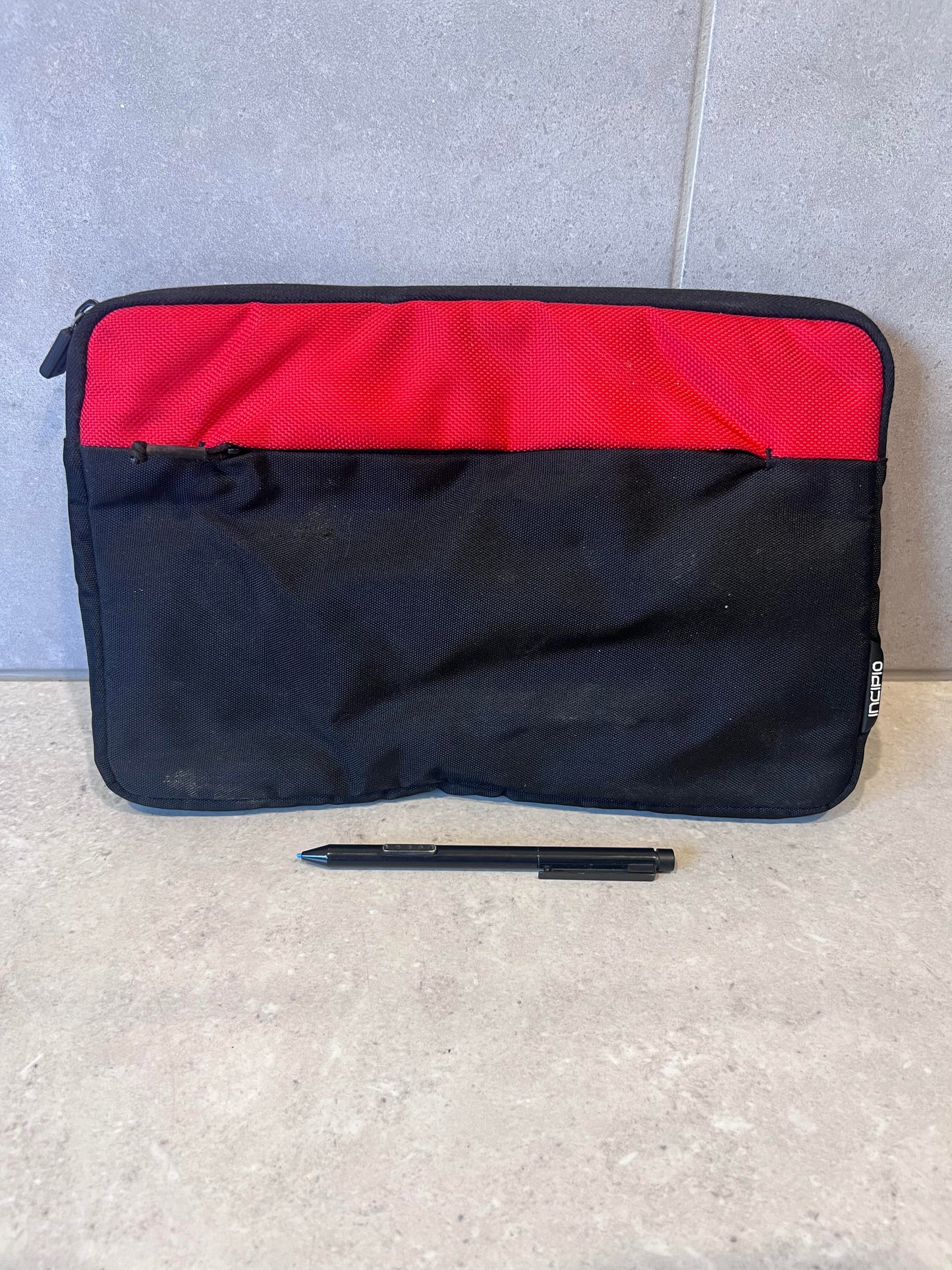 Red and black laptop sleeve case with front pocket and pen for scale