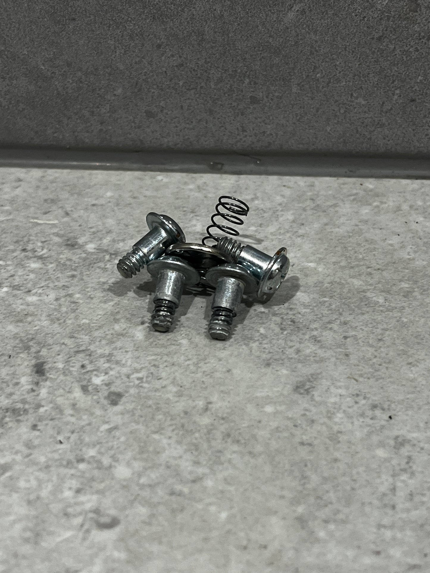Set of metal screws and small coil spring on gray surface