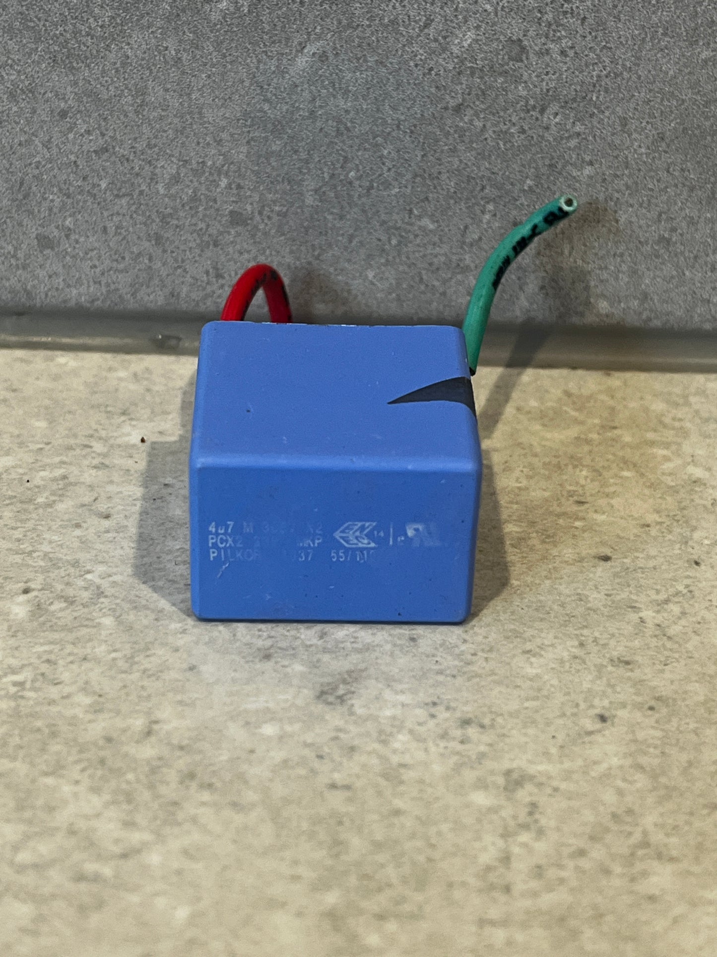 Blue film capacitor with red and green lead wires on gray surface