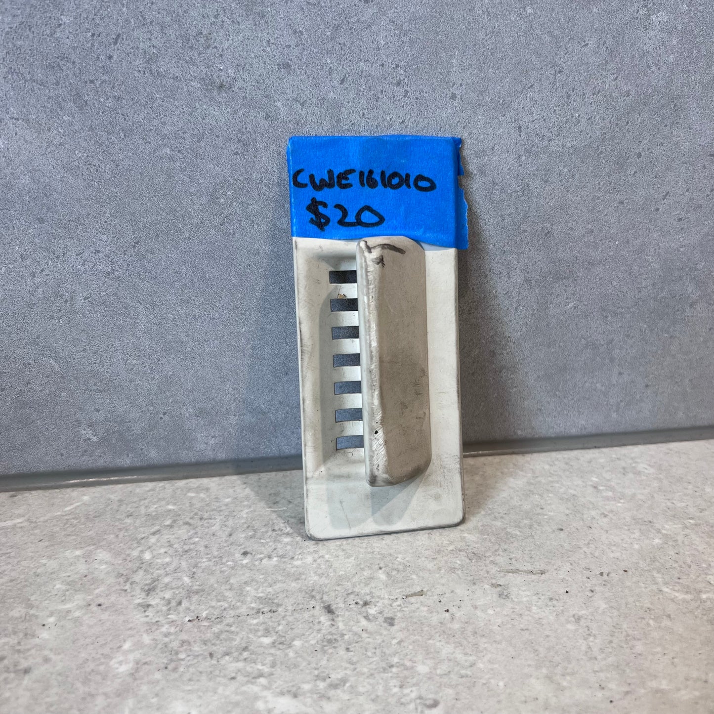 Metal louvered wall vent cover standing against a gray surface