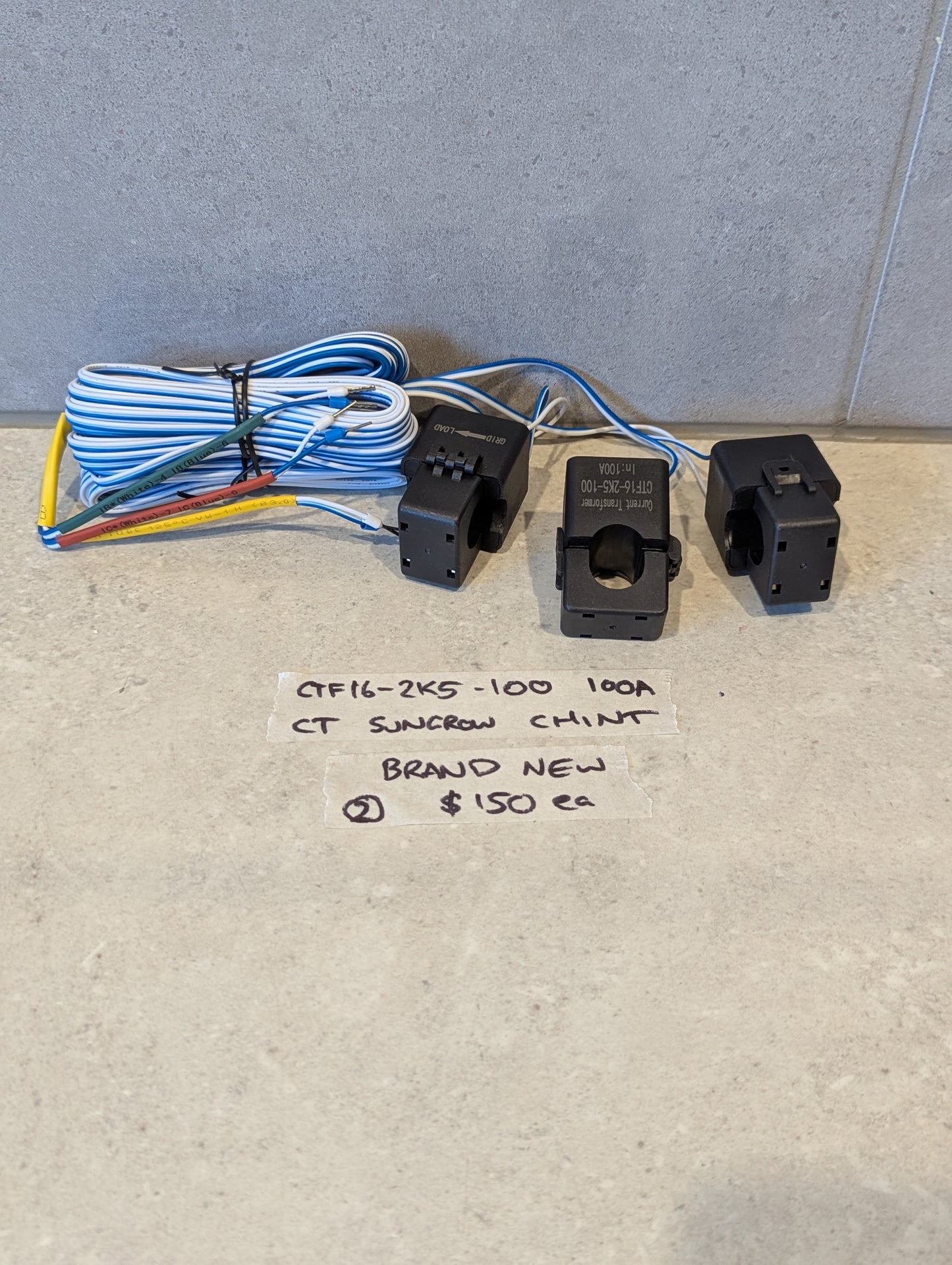 Sungrow Chint CTF16-2K5-100 current transformers with attached wires on a concrete surface and handwritten product details note