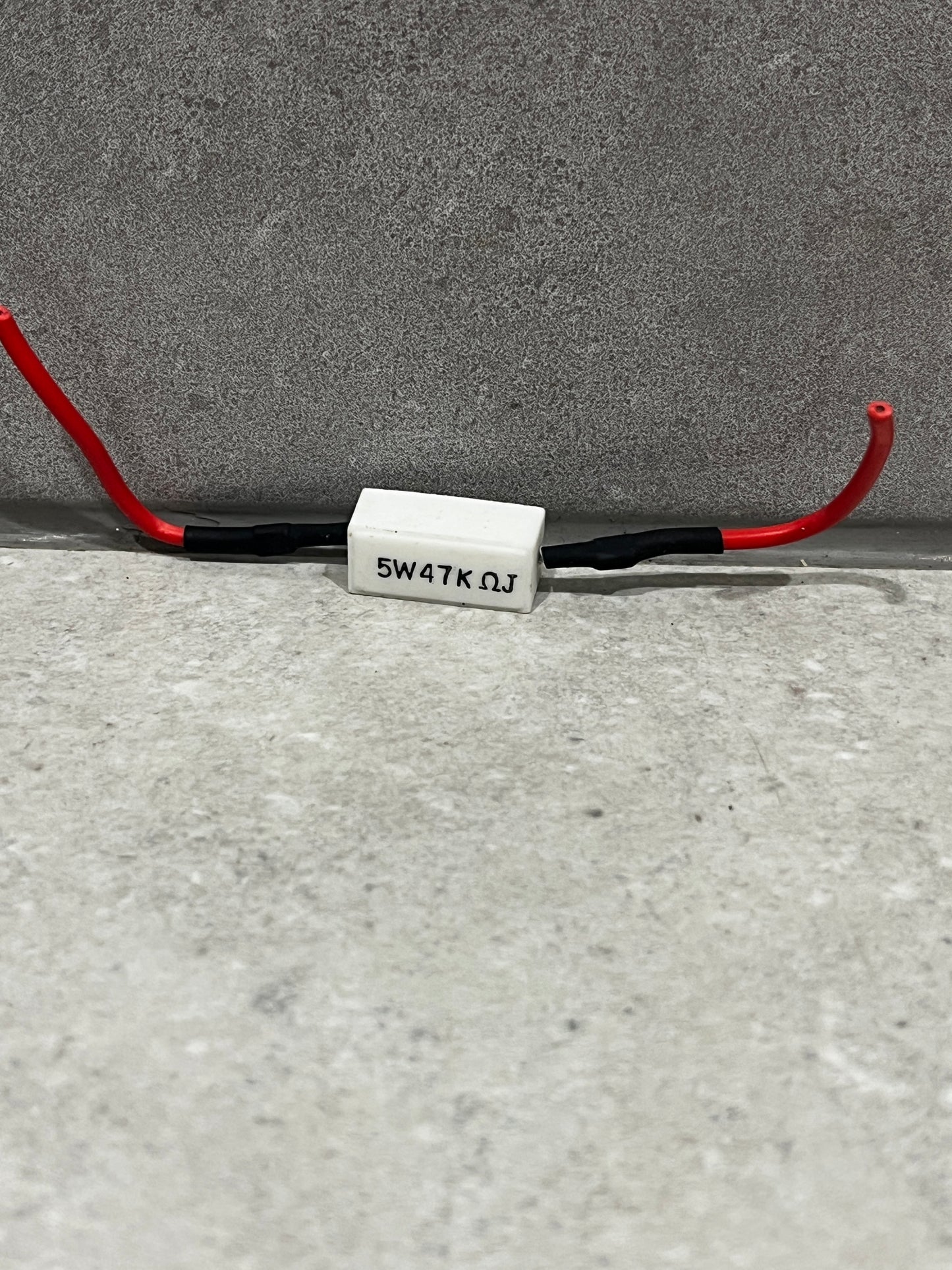 5 watt 47 kilo-ohm ceramic resistor with red insulated wires on gray background