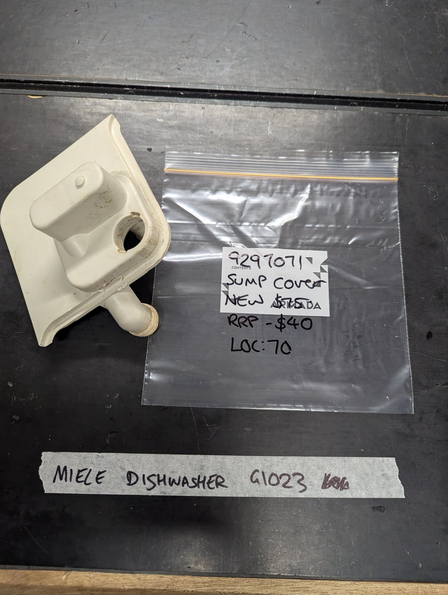 White sump cover replacement part for Miele G1023 dishwasher next to labeled plastic bag