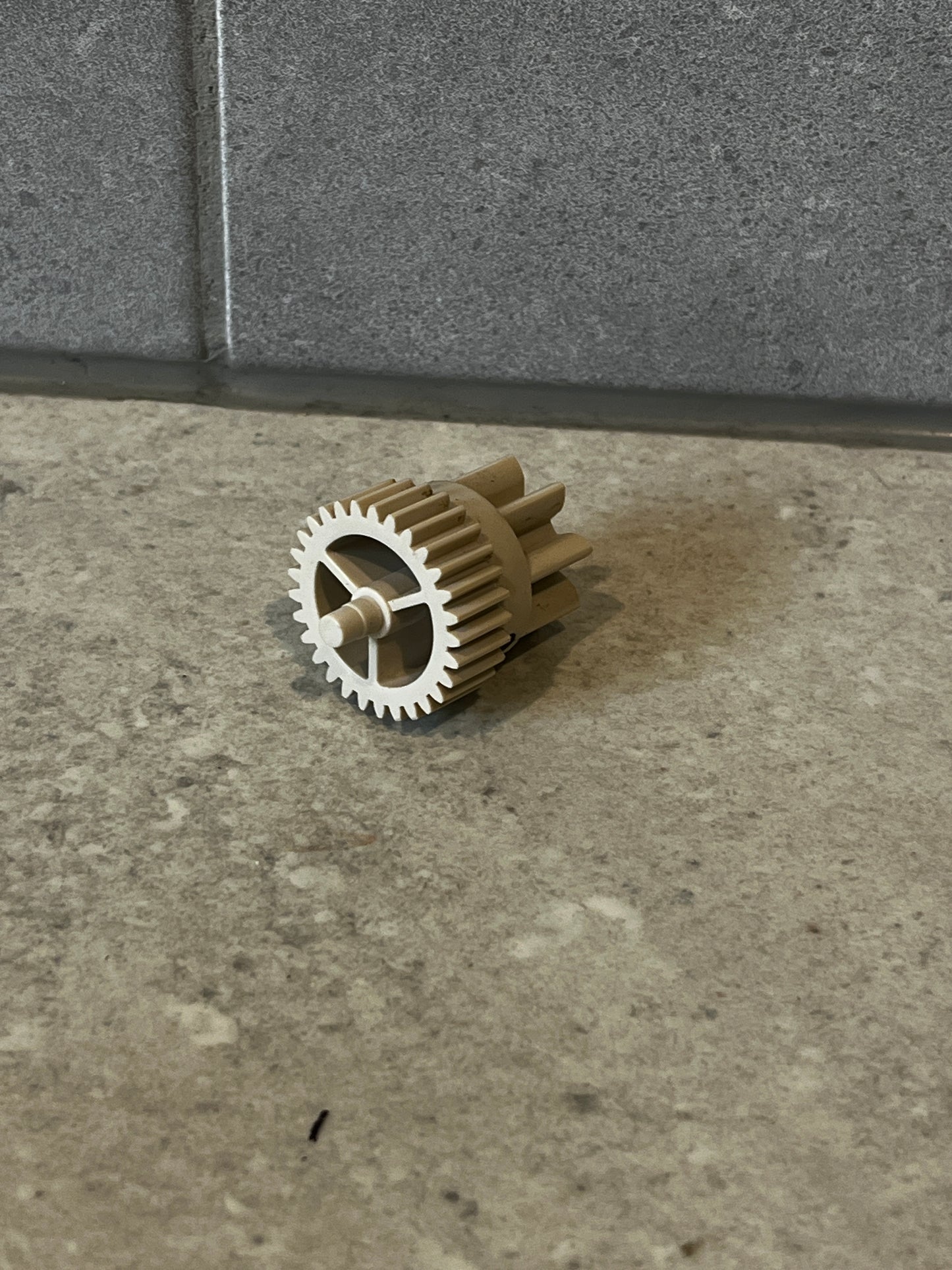 Beige plastic spur gear component on stone surface