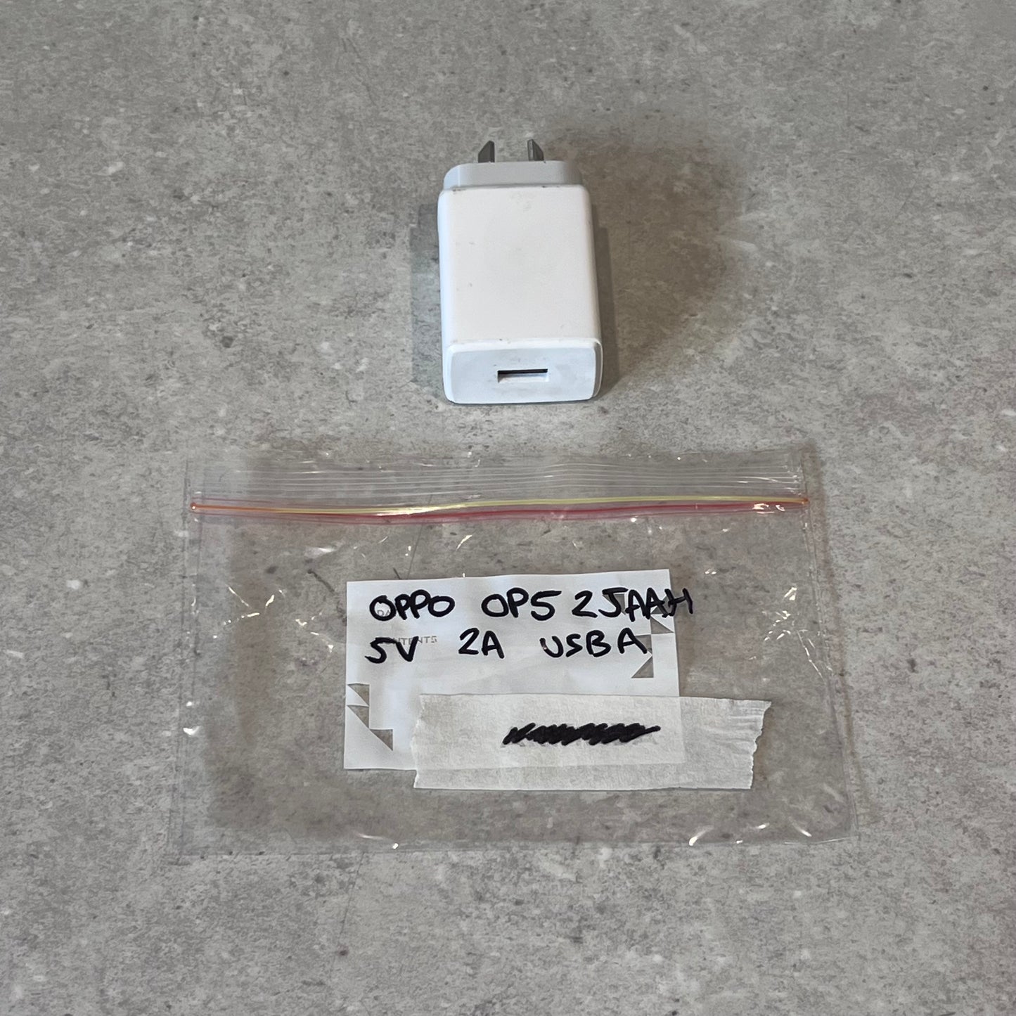 Oppo 5V 2A USB-A wall charger and labeled plastic bag on gray surface