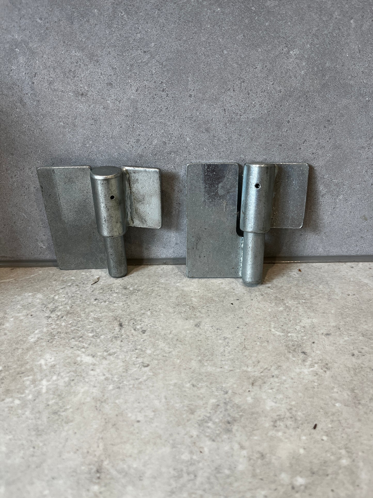 Set of two heavy-duty metal gate hinges with galvanized finish on a stone surface
