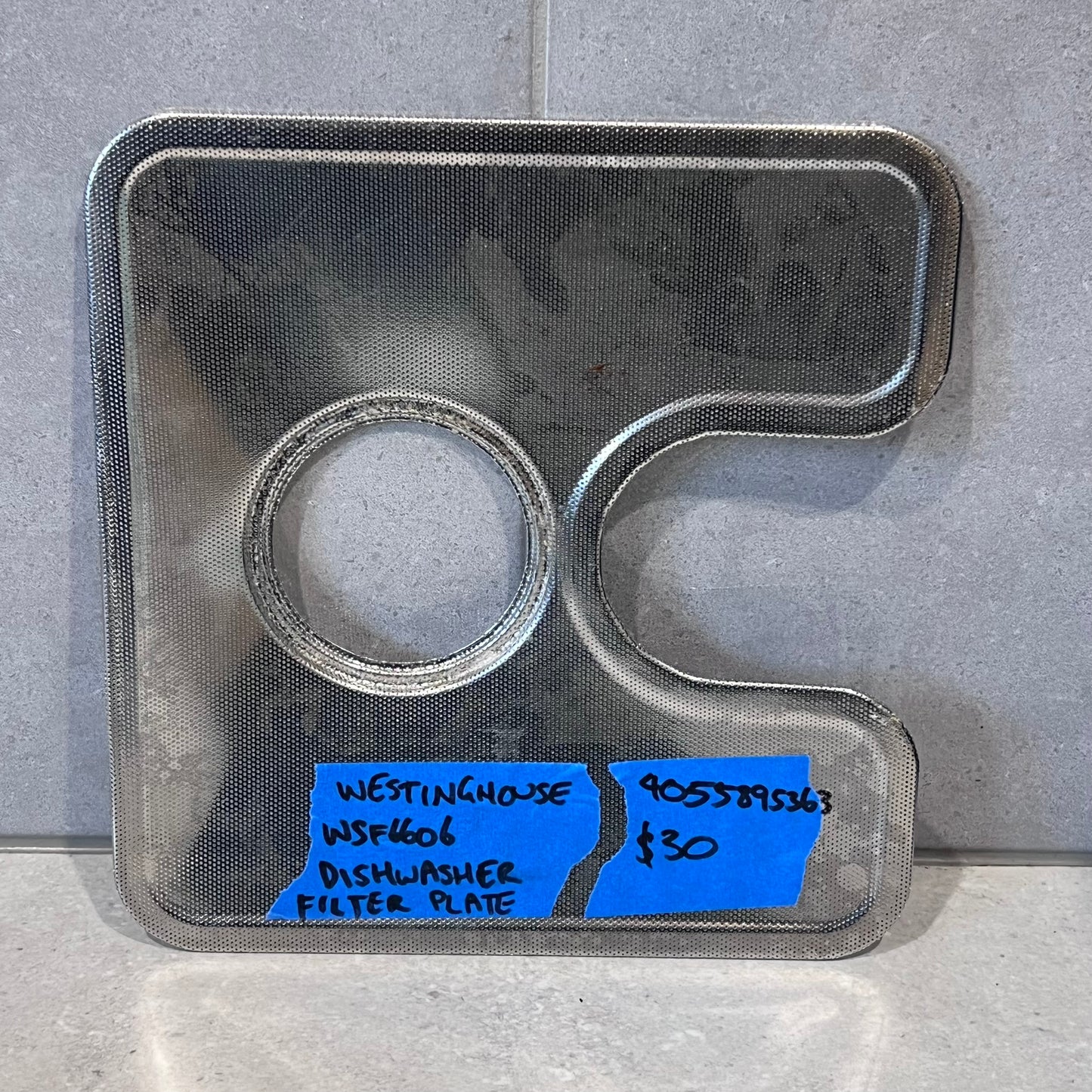 Westinghouse WSF6606 dishwasher filter plate made of metal mesh on a gray background