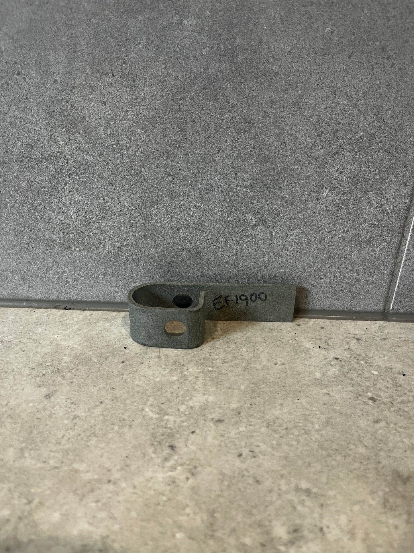 Steel mounting bracket with pre-drilled hole lying flat on a gray surface