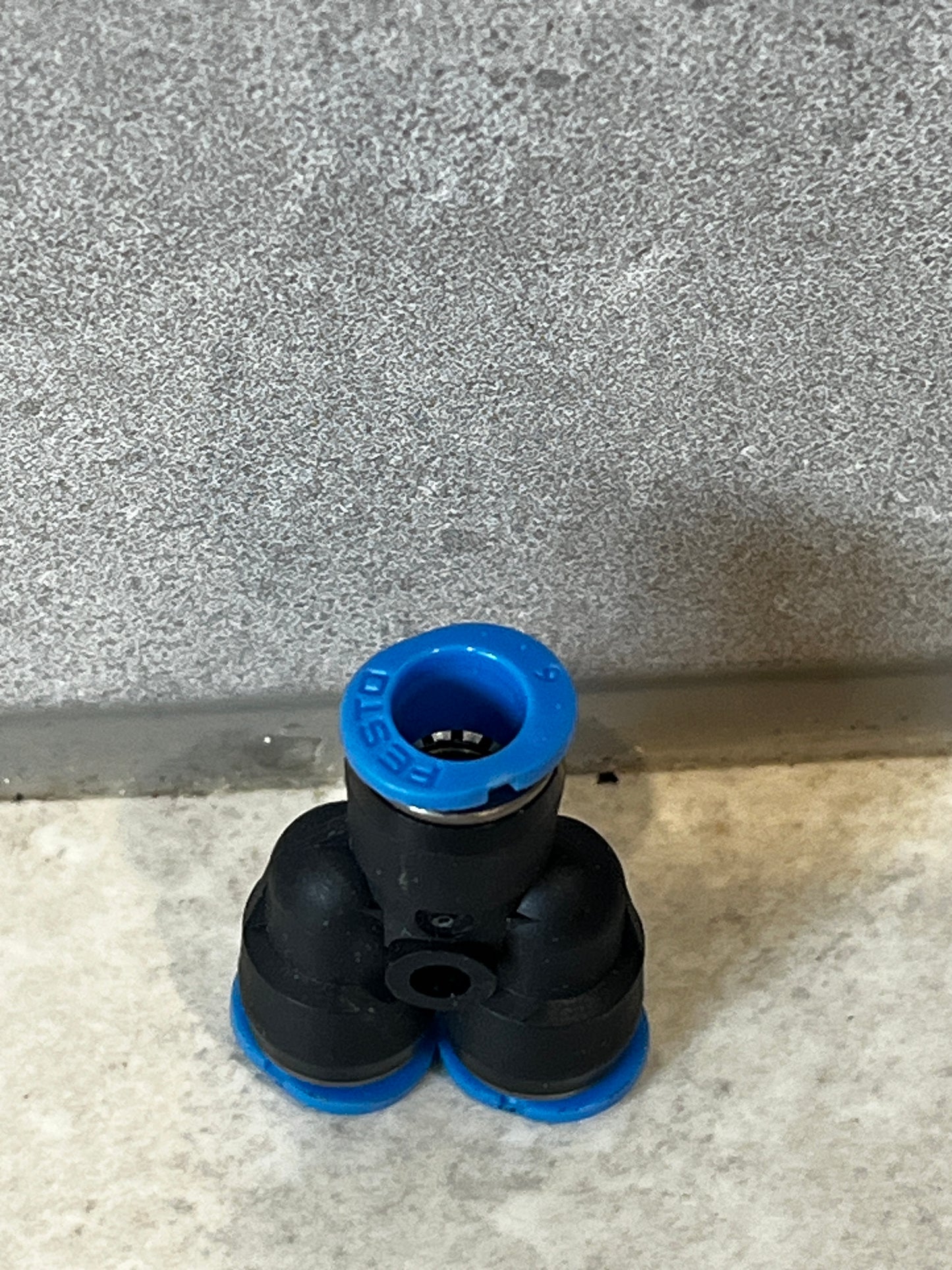 Front angle view of pneumatic Y fitting with blue Festo ring and black polymer structure on gray stone background