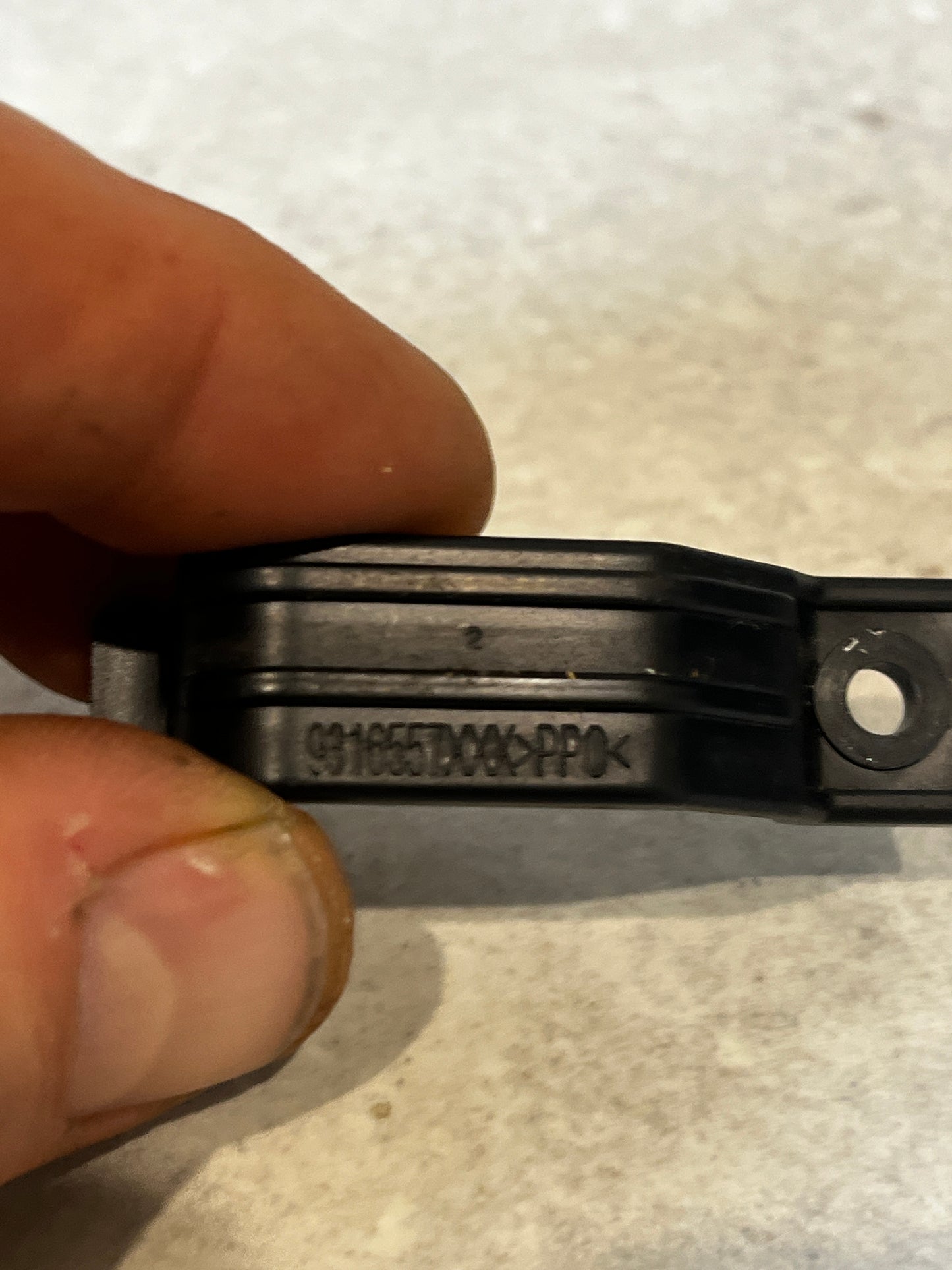 Close-up of black plastic mounting bracket clip with part number