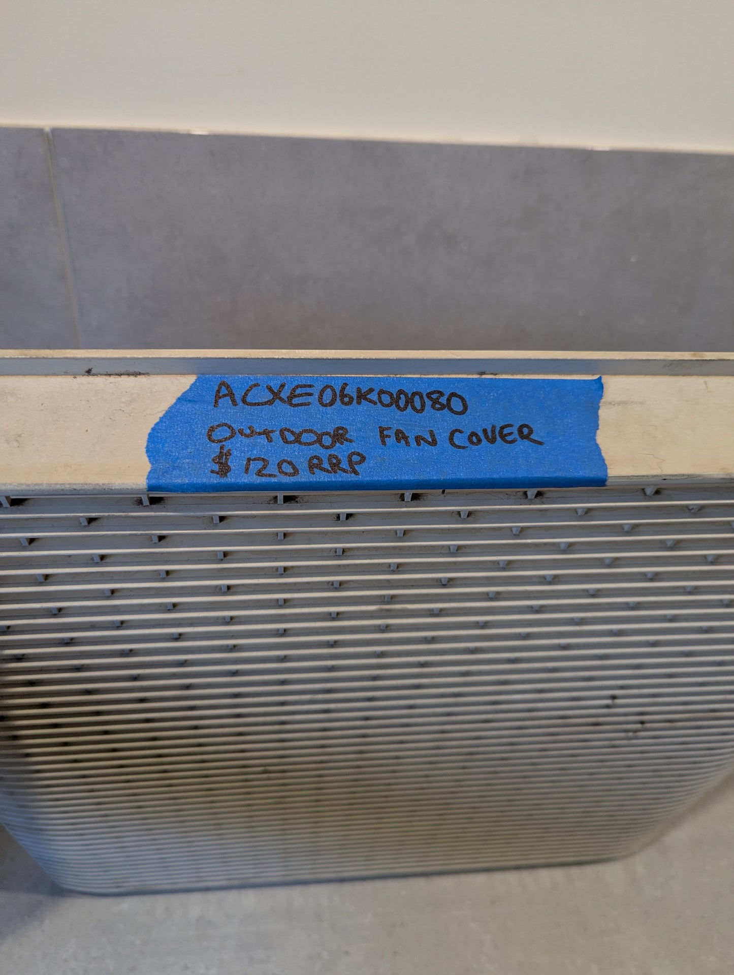 Close-up of outdoor fan cover grille with handwritten label showing product code and price