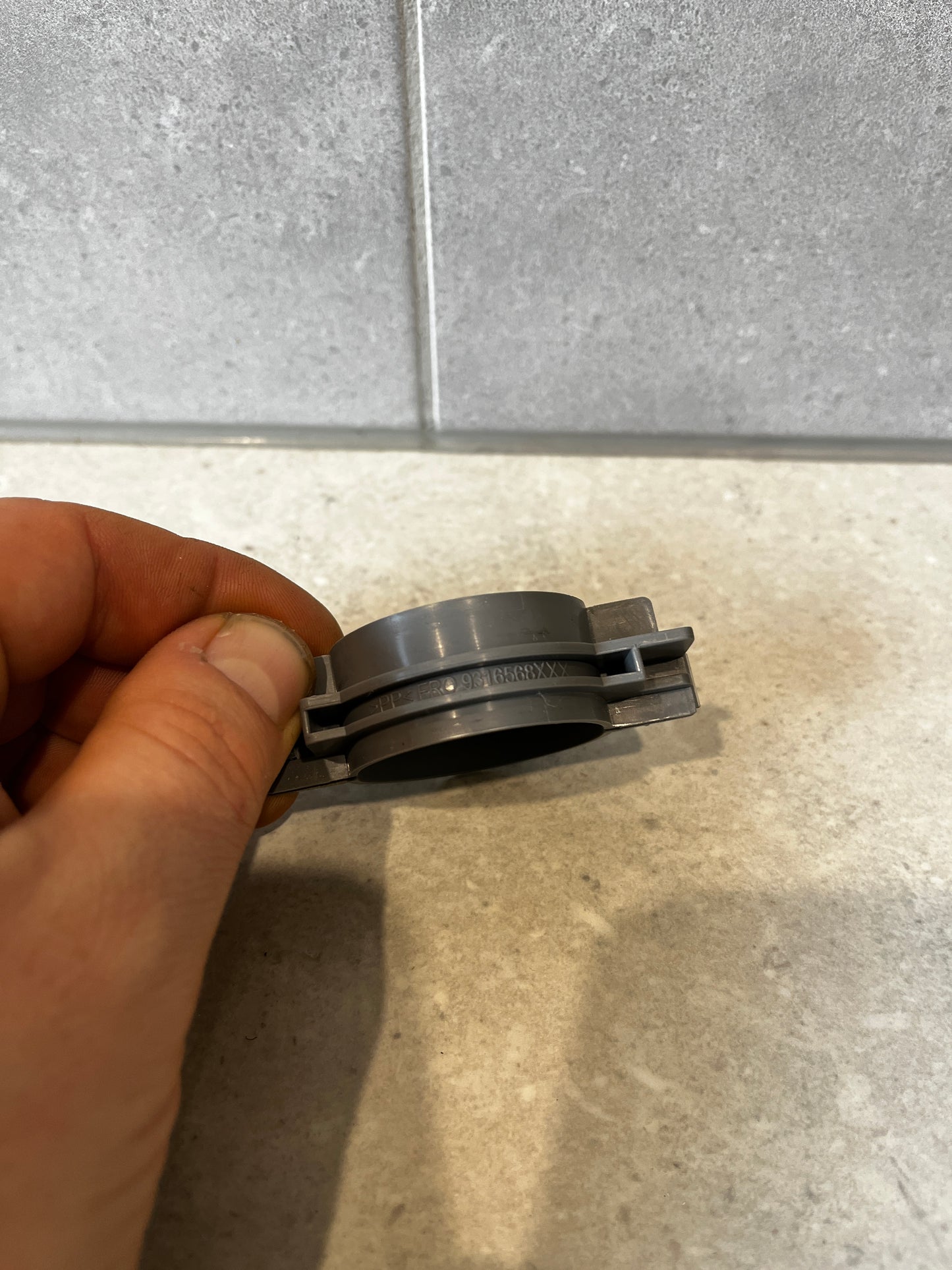 Hand holding a side view of a gray plastic connector fitting, showcasing detailed construction