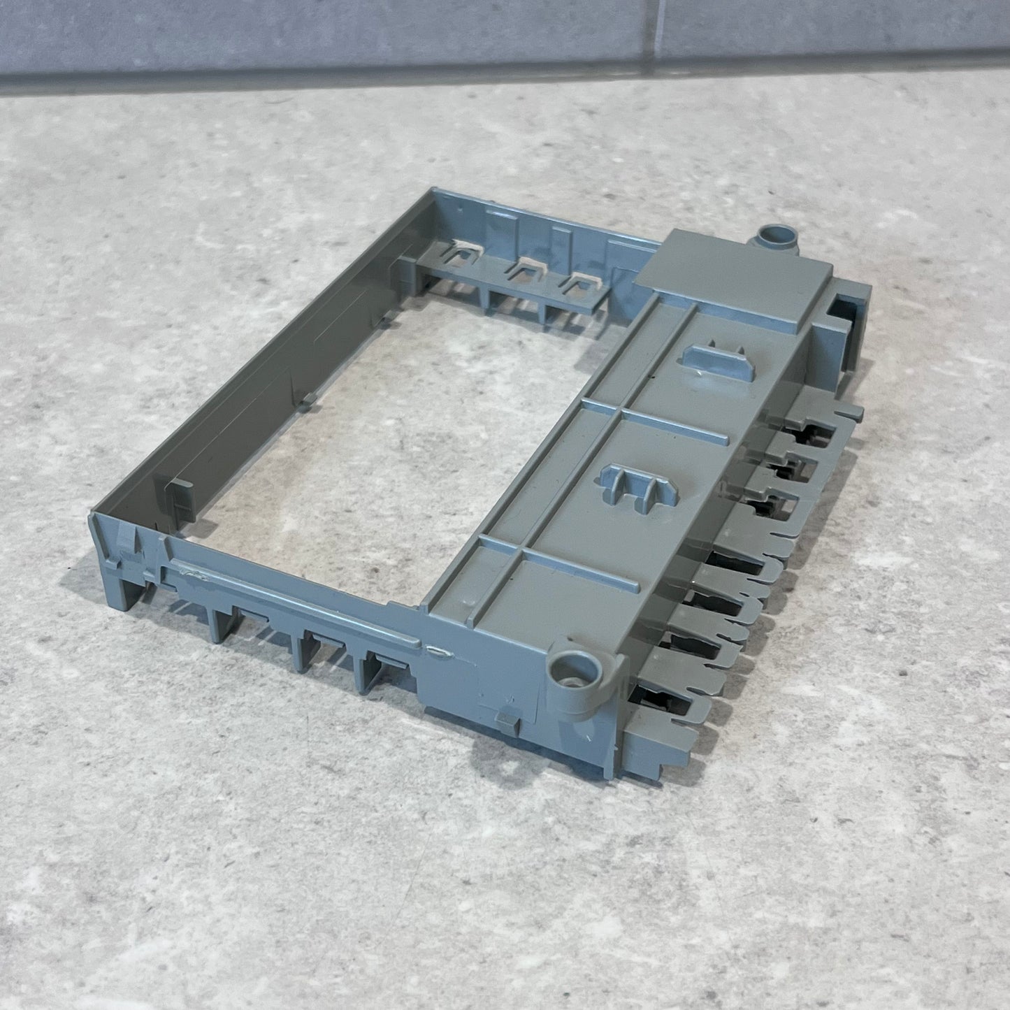 Angled view of gray plastic mid frame for PCB display box on gray surface