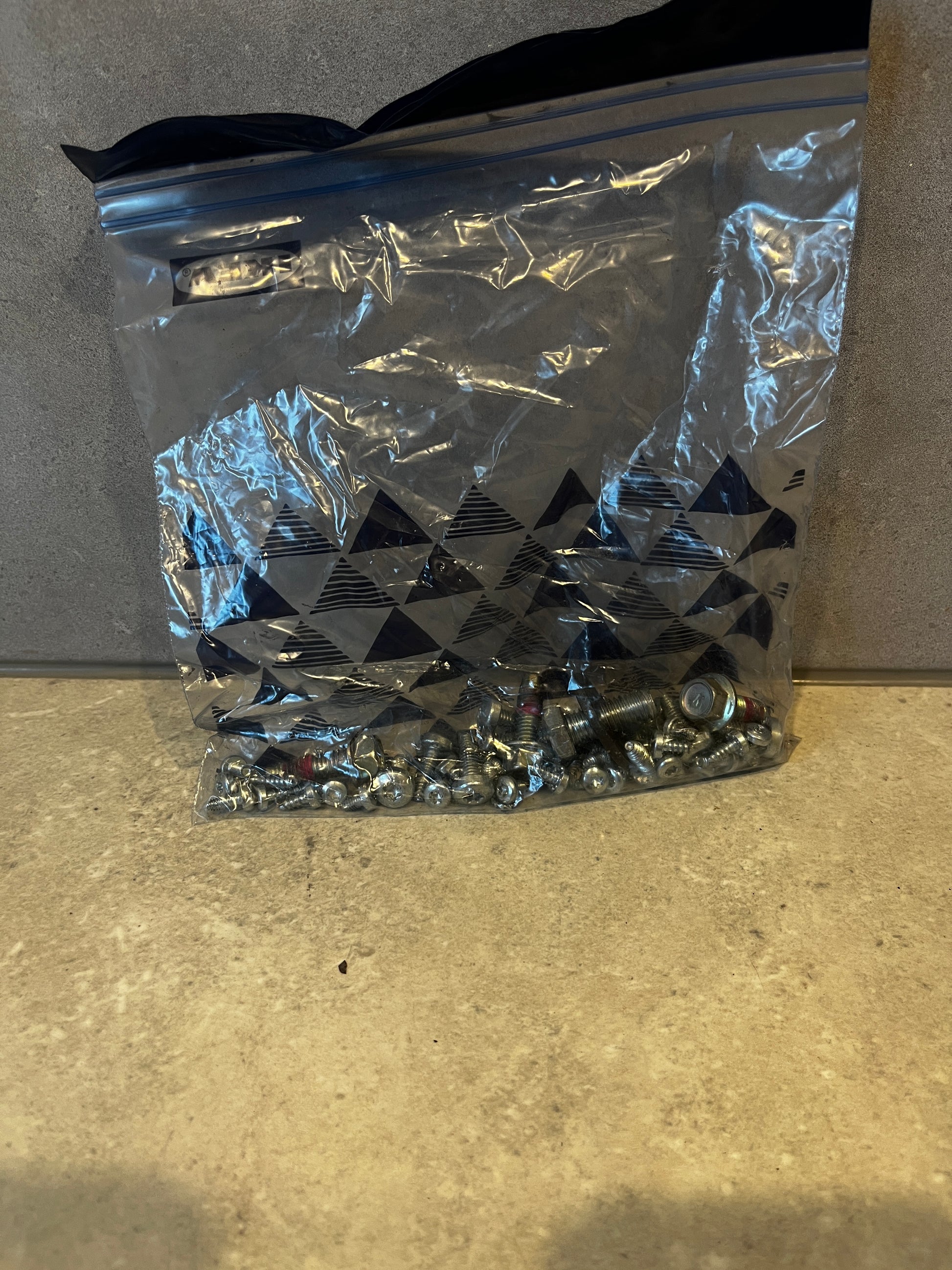 Assorted metal bolts and nuts in a resealable plastic bag on a countertop