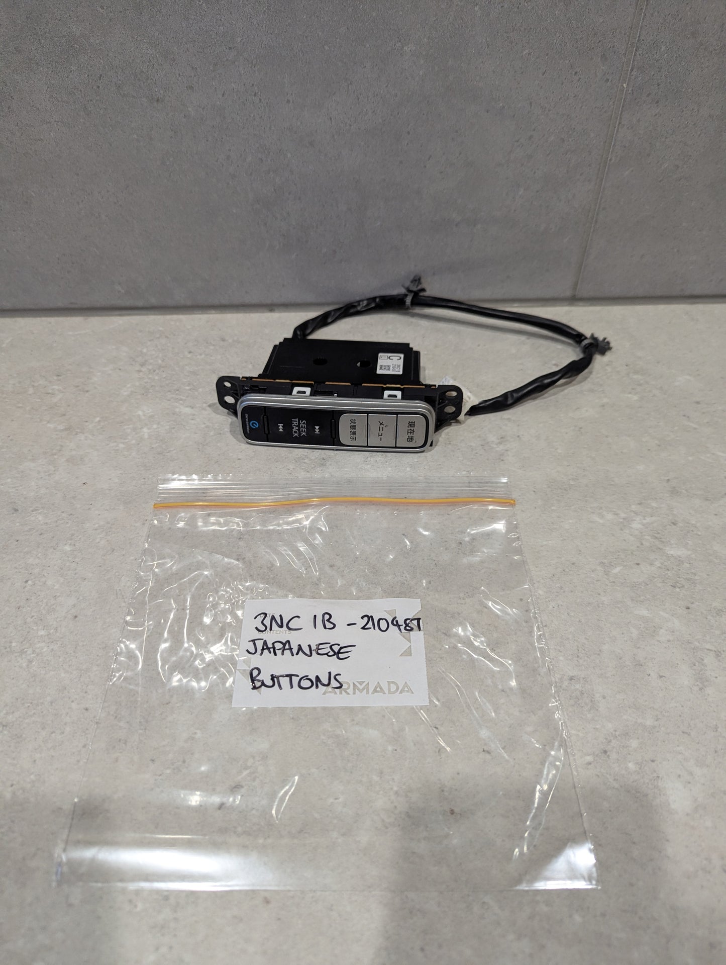Japanese button automotive control switch panel with wiring on a countertop next to labeled plastic bag