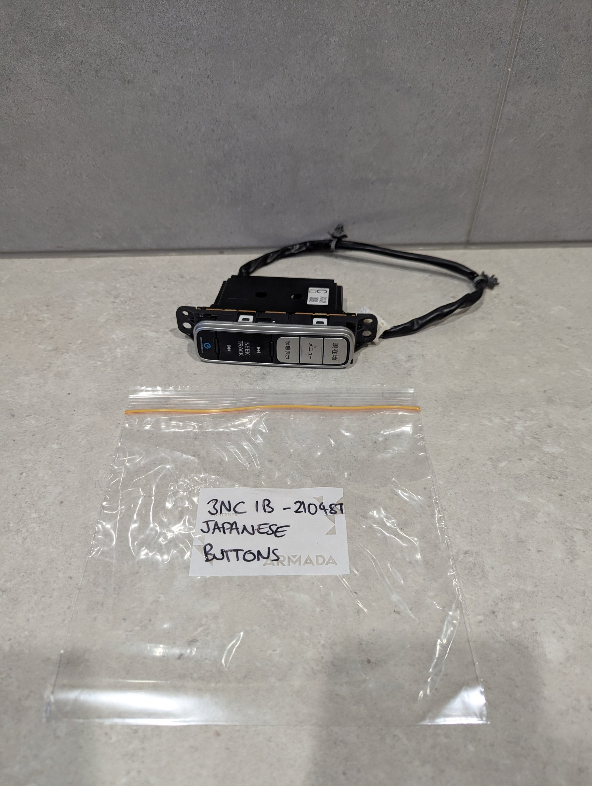 Japanese button automotive control switch panel with wiring on a countertop next to labeled plastic bag