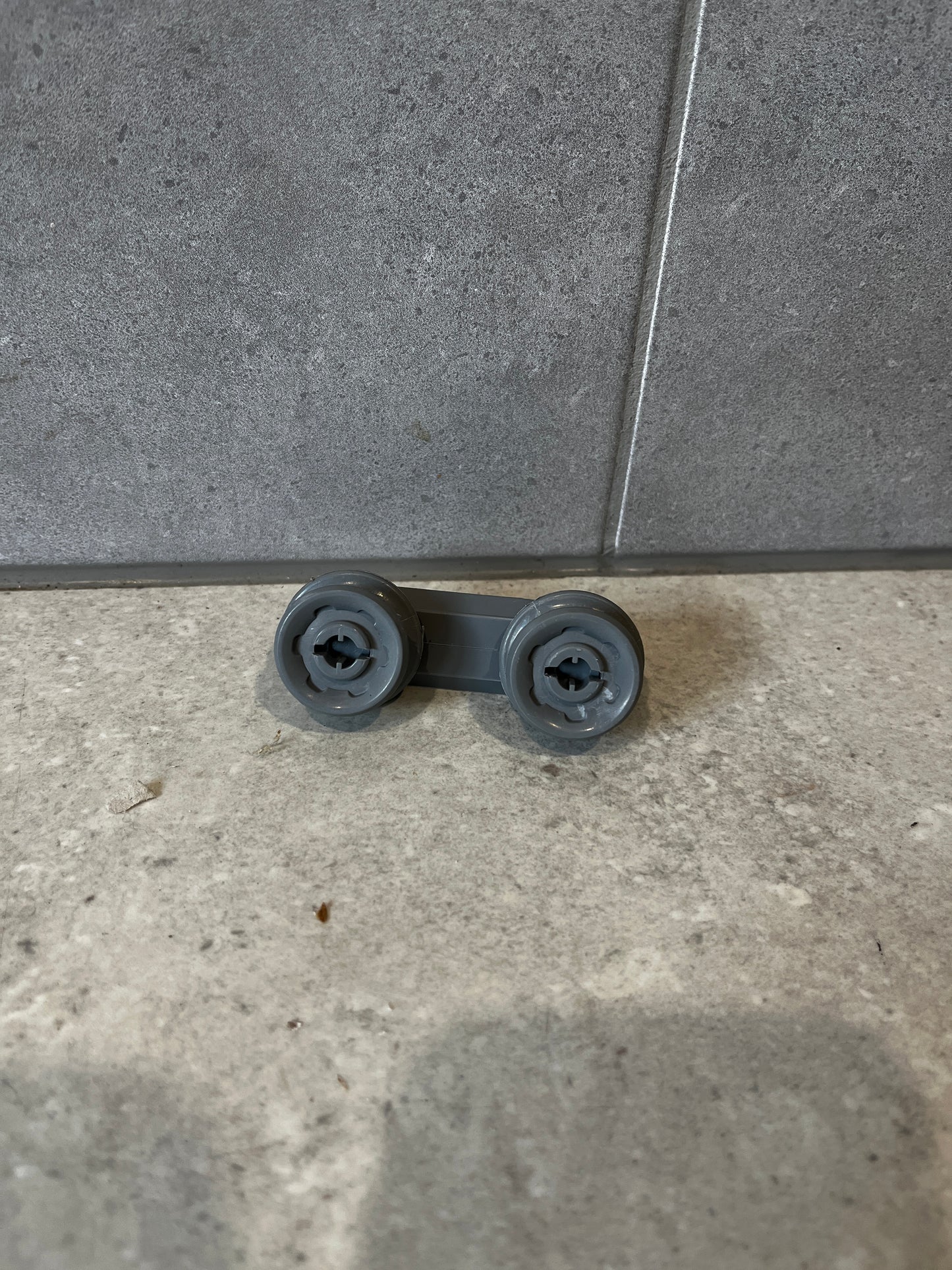 Gray dishwasher rack roller wheel assembly on tile background