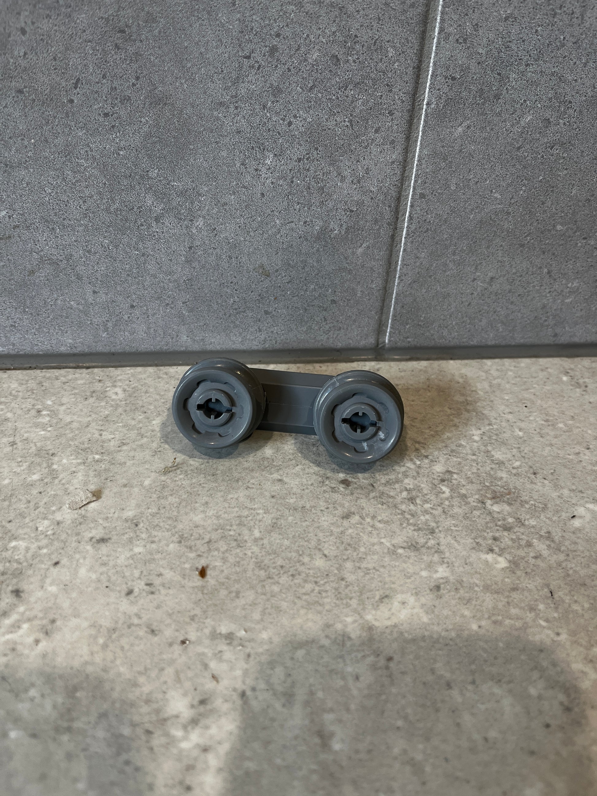 Gray dishwasher rack roller wheel assembly on tile background