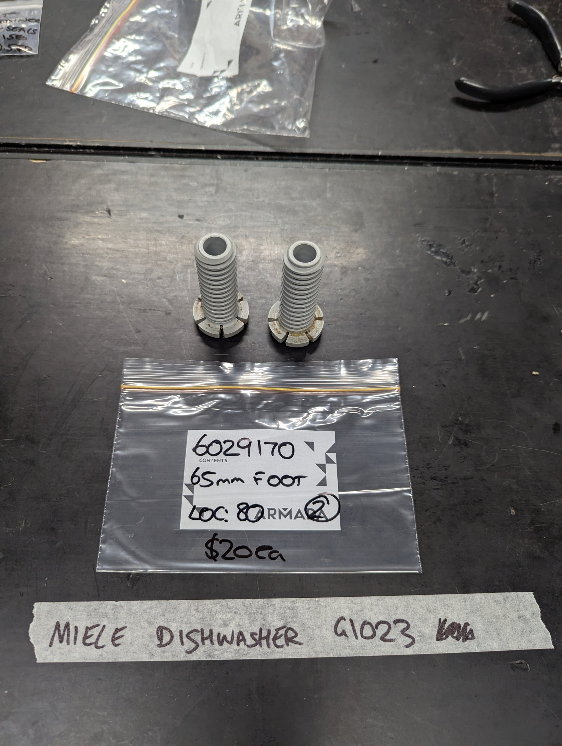 Pair of Miele dishwasher 65mm feet and labeled packaging displayed on a workbench
