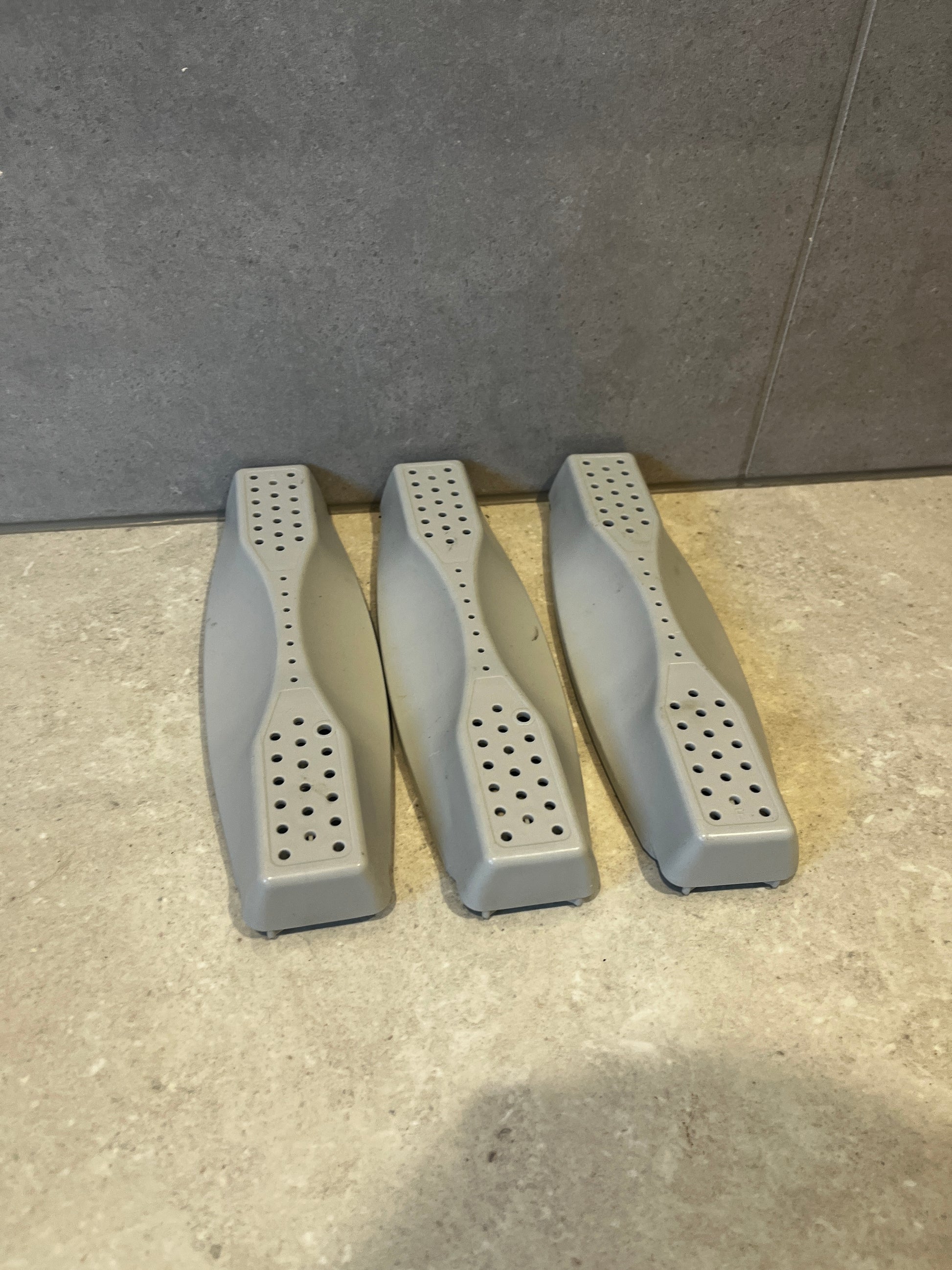 Three gray dishwasher rack roller assemblies on a stone surface