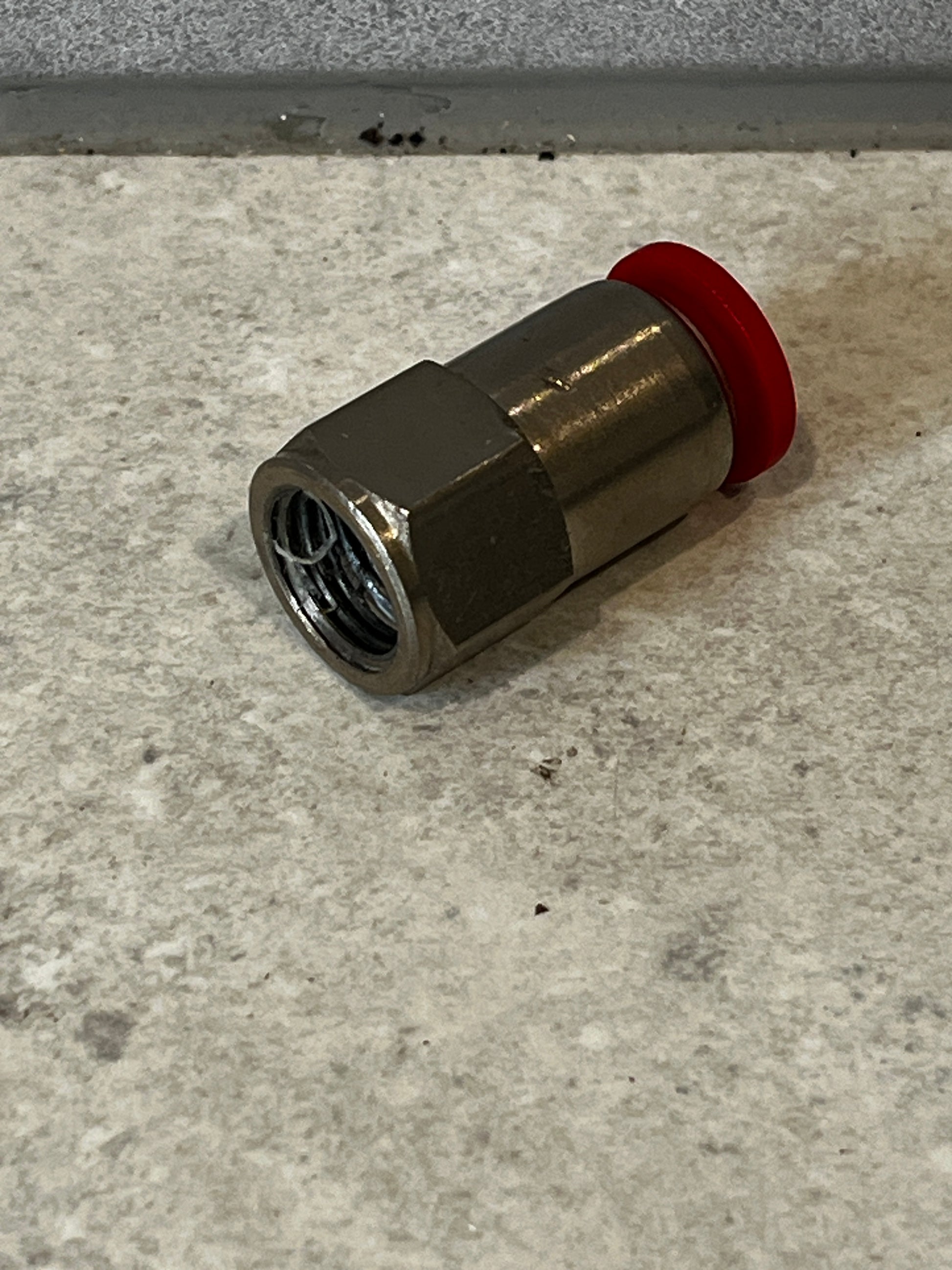 Coaxial cable compression connector with red compression ring lying on floor