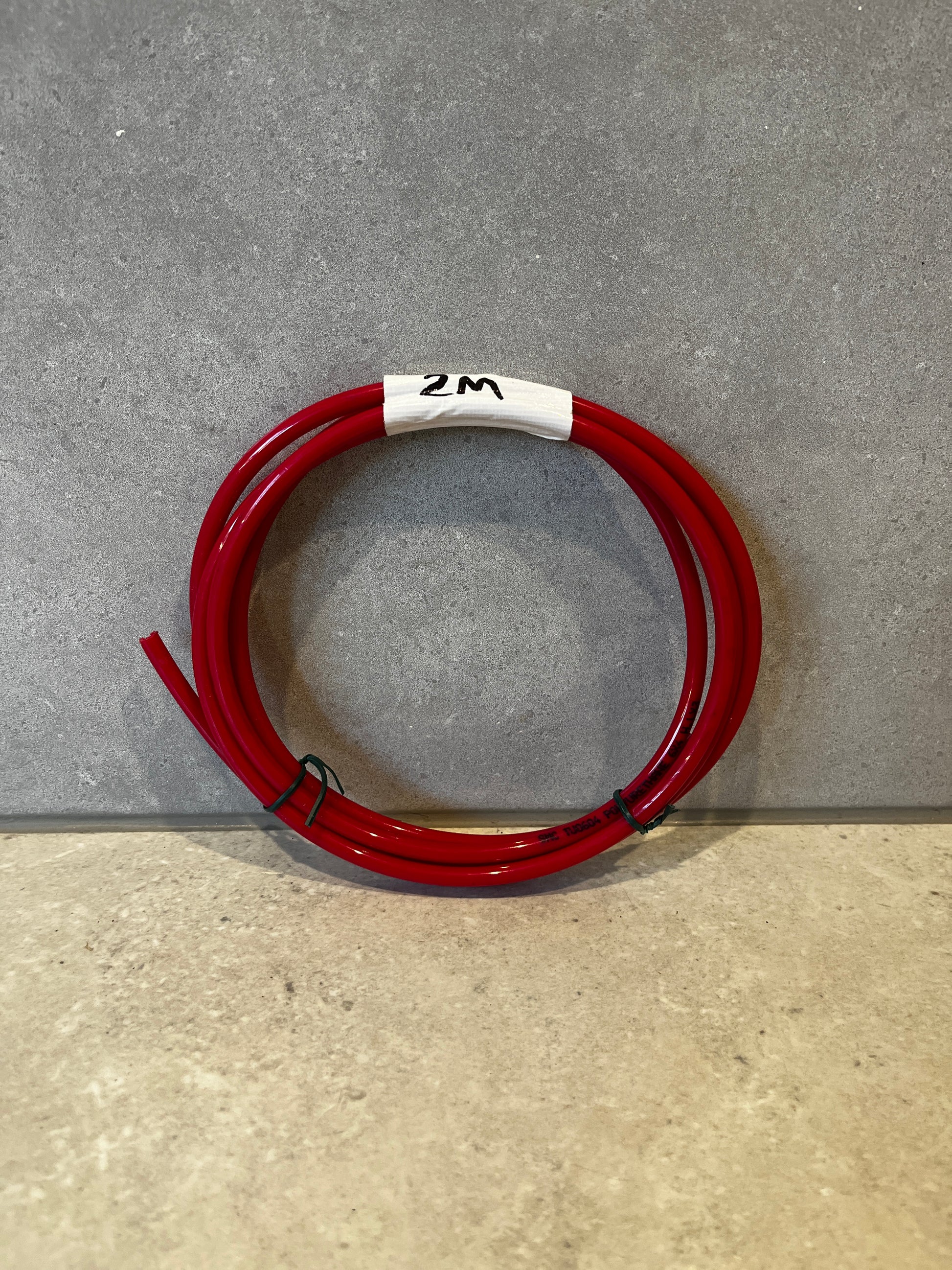 Coiled red polyurethane tubing labeled 2 meters on a grey surface