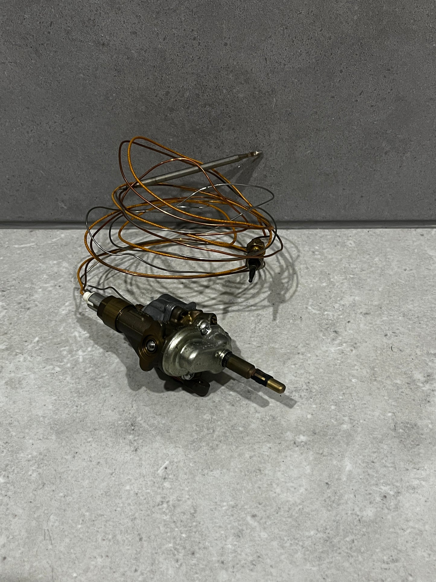 Gas oven thermostat control valve with copper sensing coil on gray surface