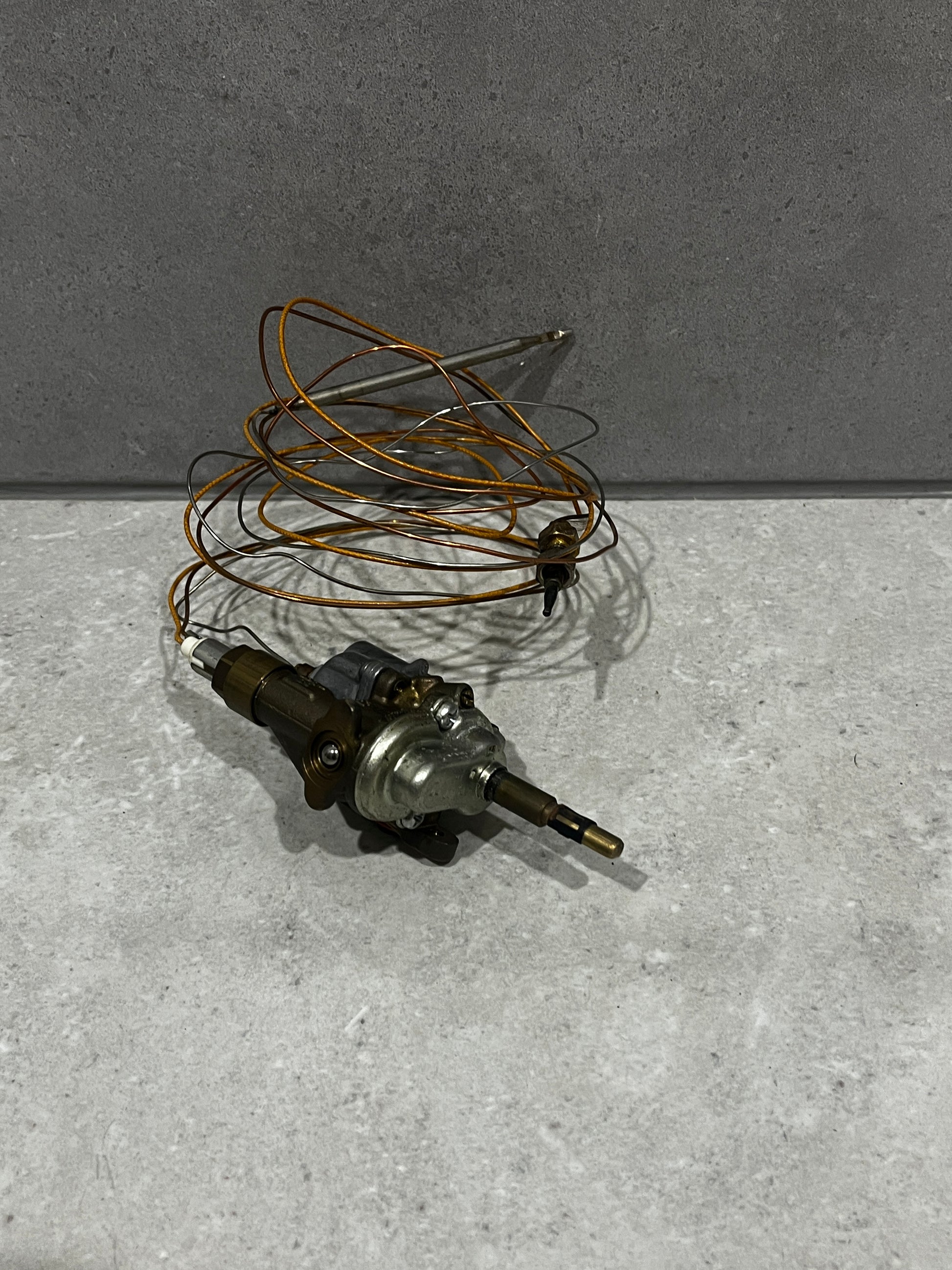 Gas oven thermostat control valve with copper sensing coil on gray surface