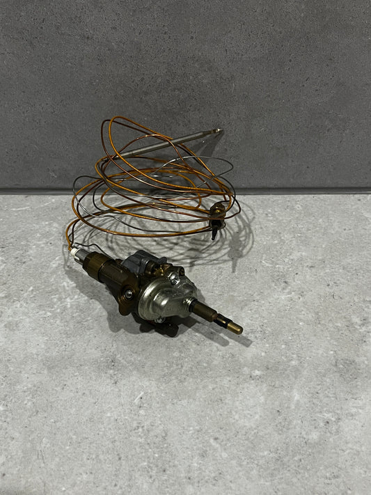 Gas oven thermostat control valve with copper sensing coil on gray surface
