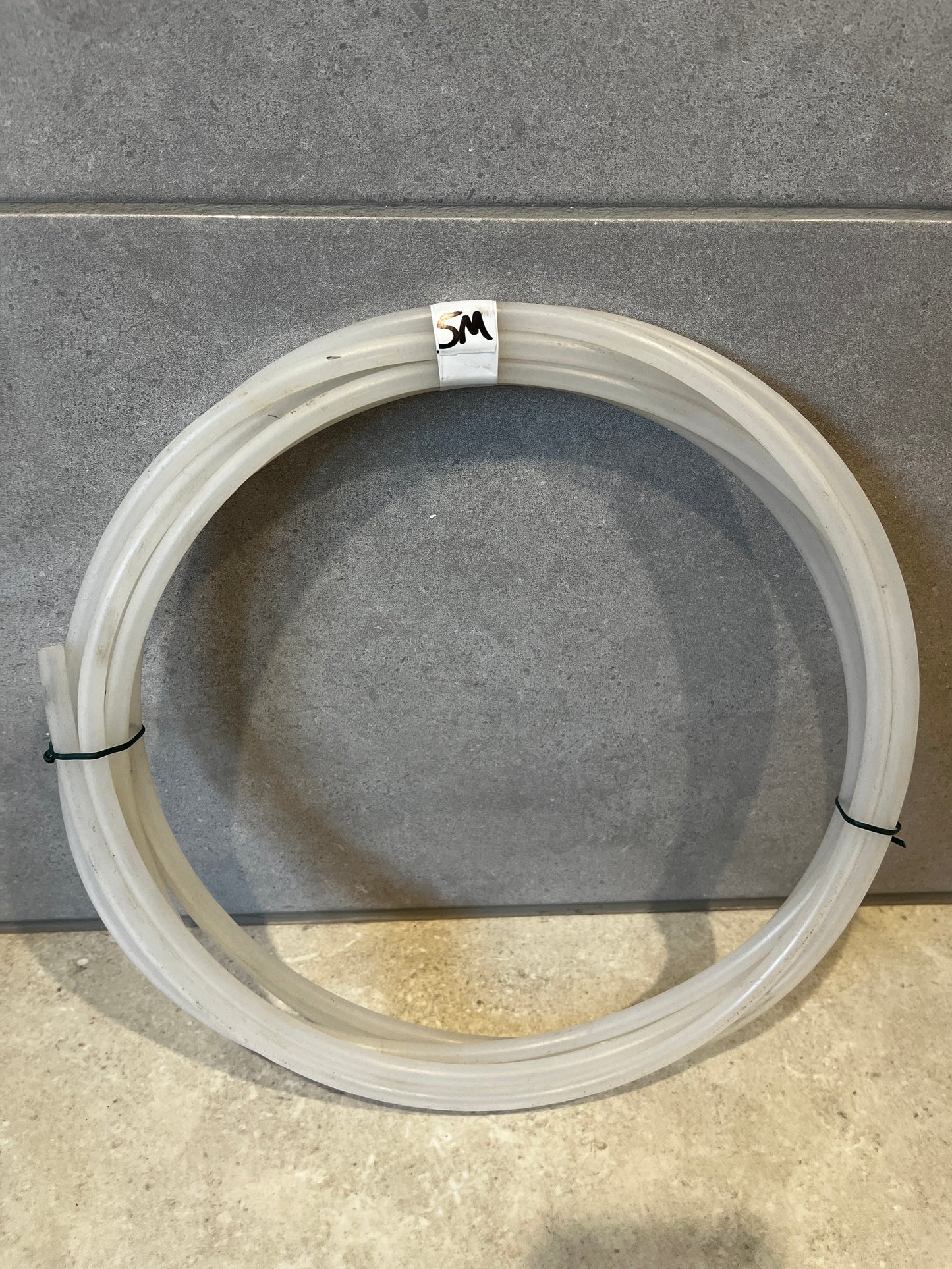 Coiled clear silicone tubing with 5M label on tiled floor background
