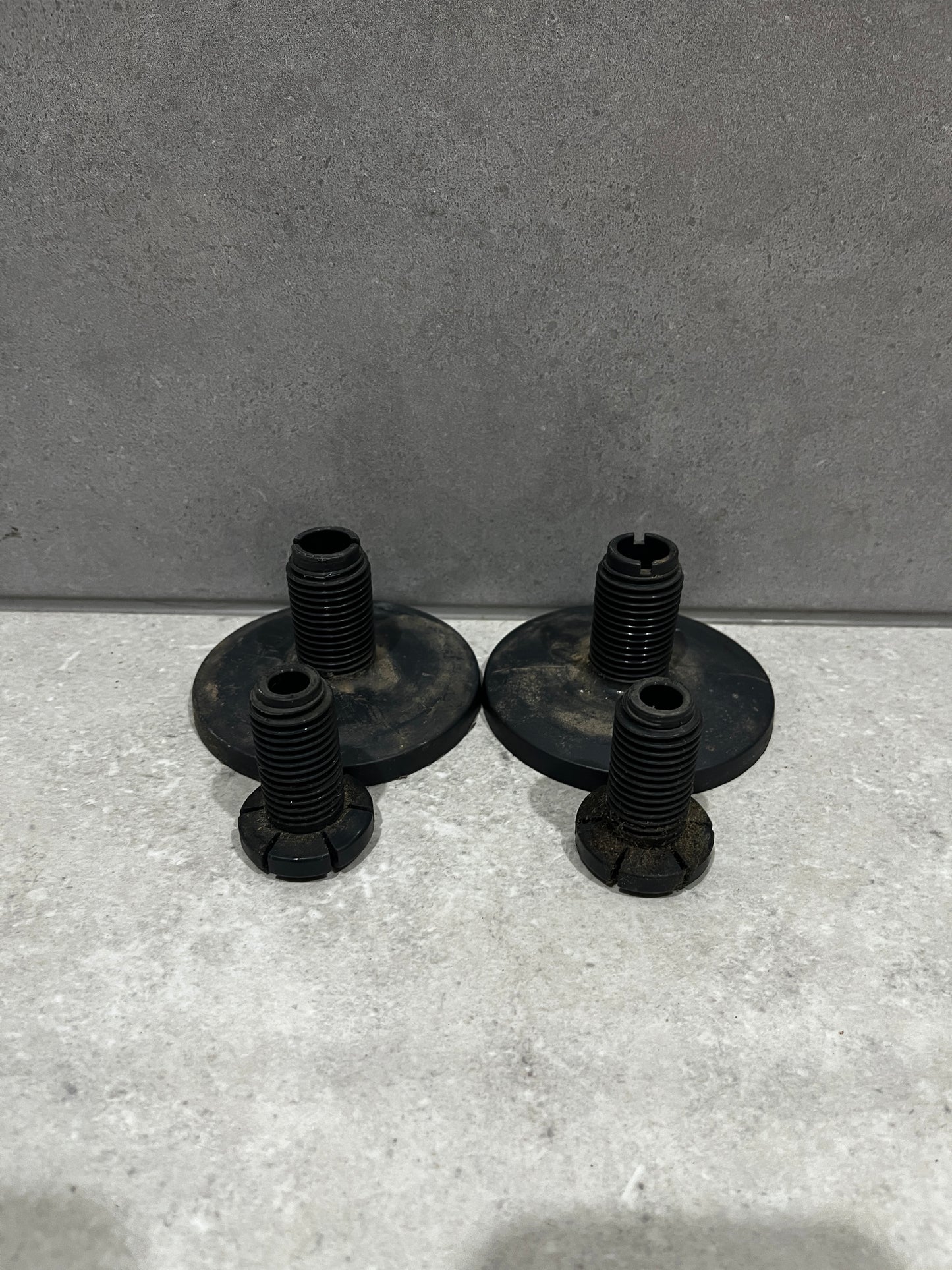set of four black metal furniture leveling feet with threaded bolts and wide base plates on concrete background