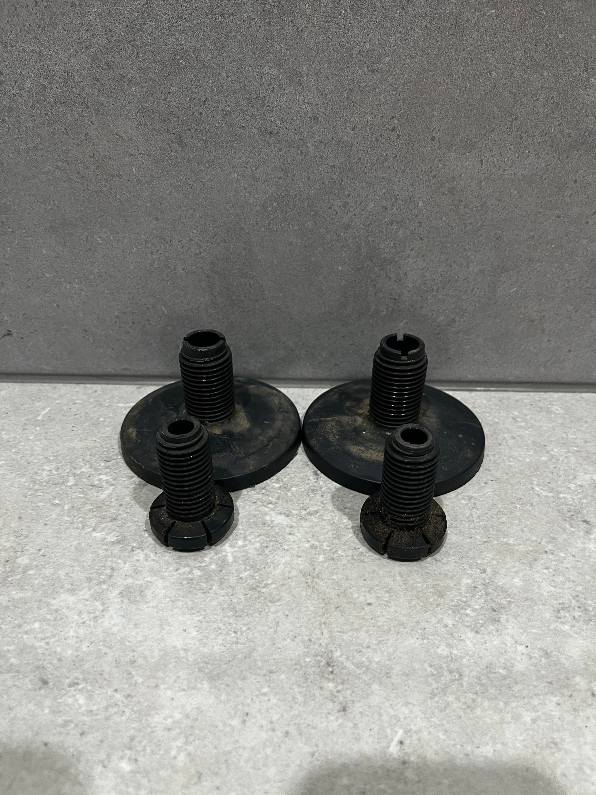 set of four black metal furniture leveling feet with threaded bolts and wide base plates on concrete background