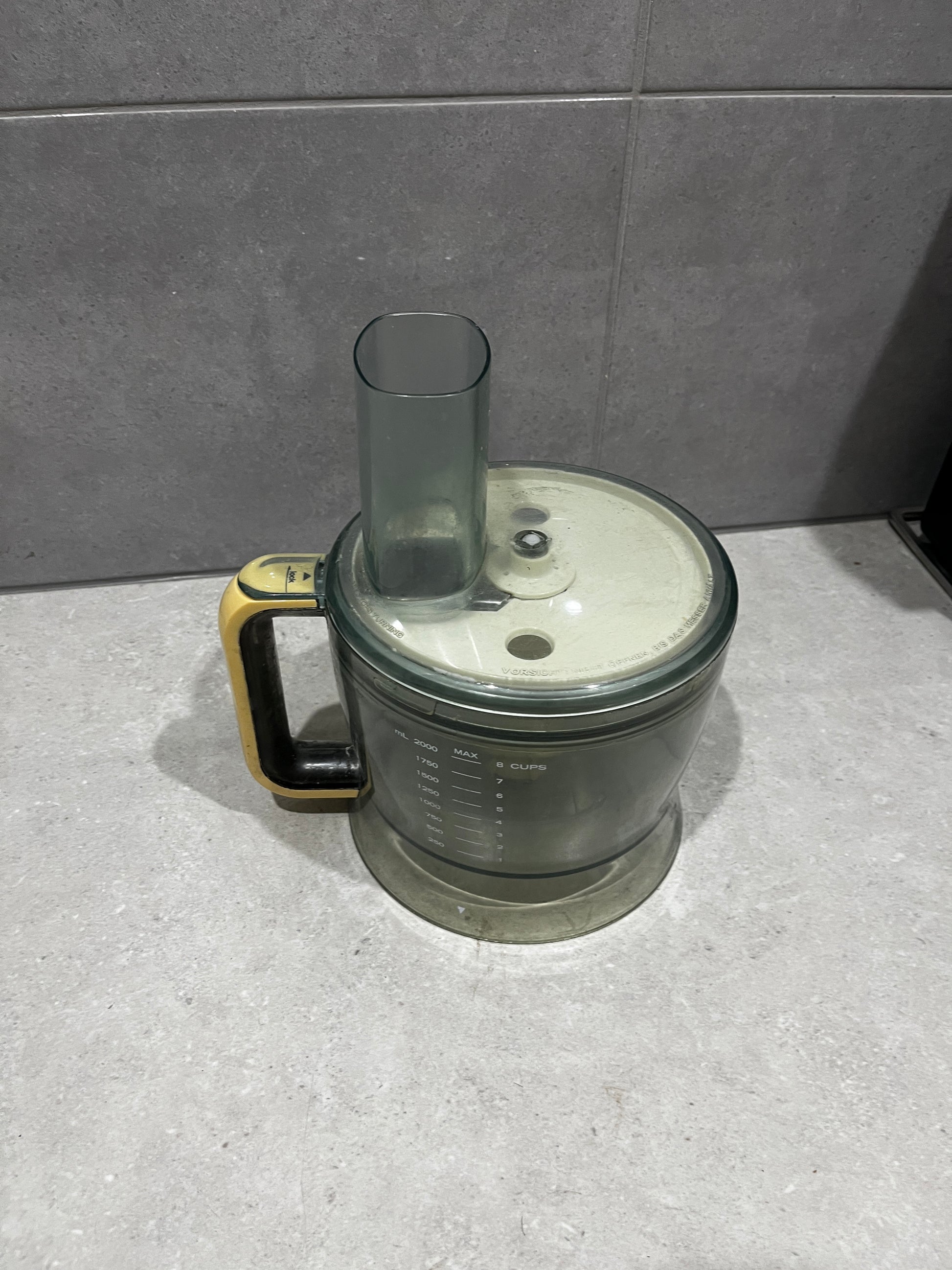 Food processor bowl with translucent dark plastic and yellow-black handle on countertop