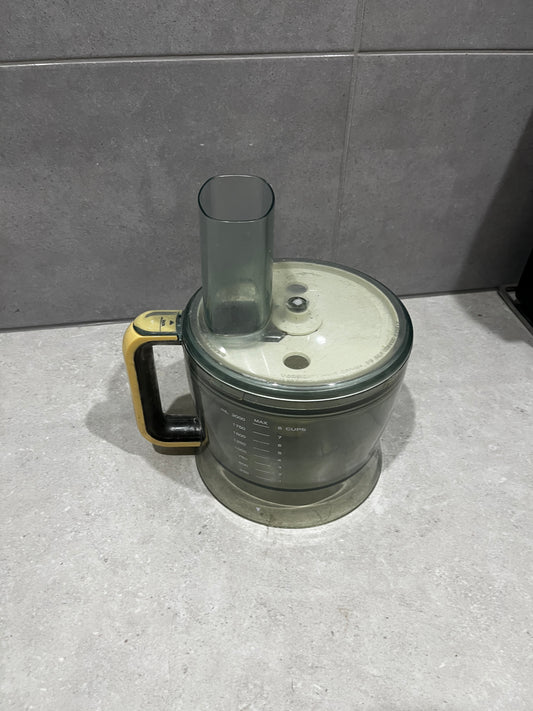 Food processor bowl with translucent dark plastic and yellow-black handle on countertop