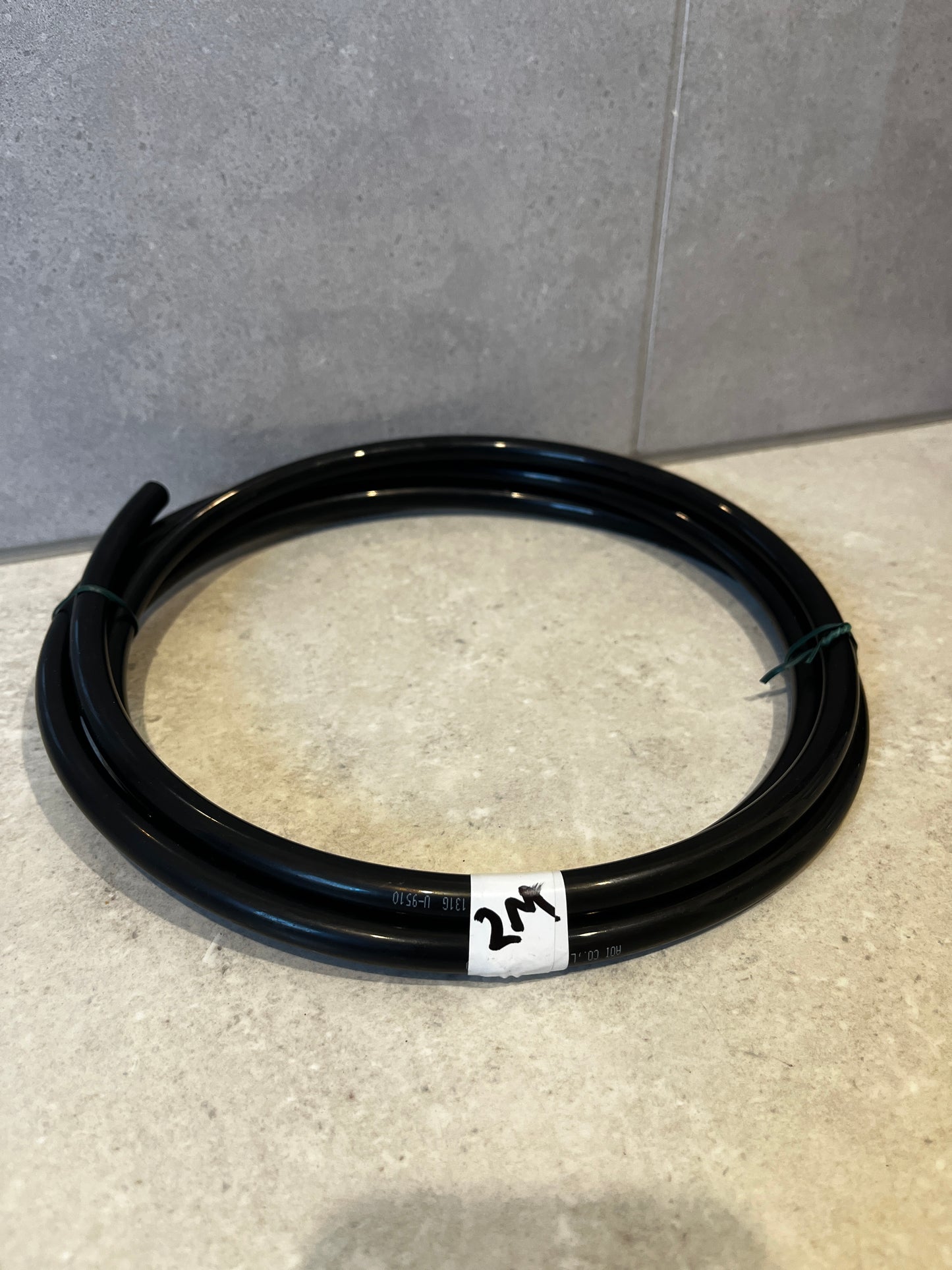 Coiled black flexible tubing with white 2M label on tiled surface