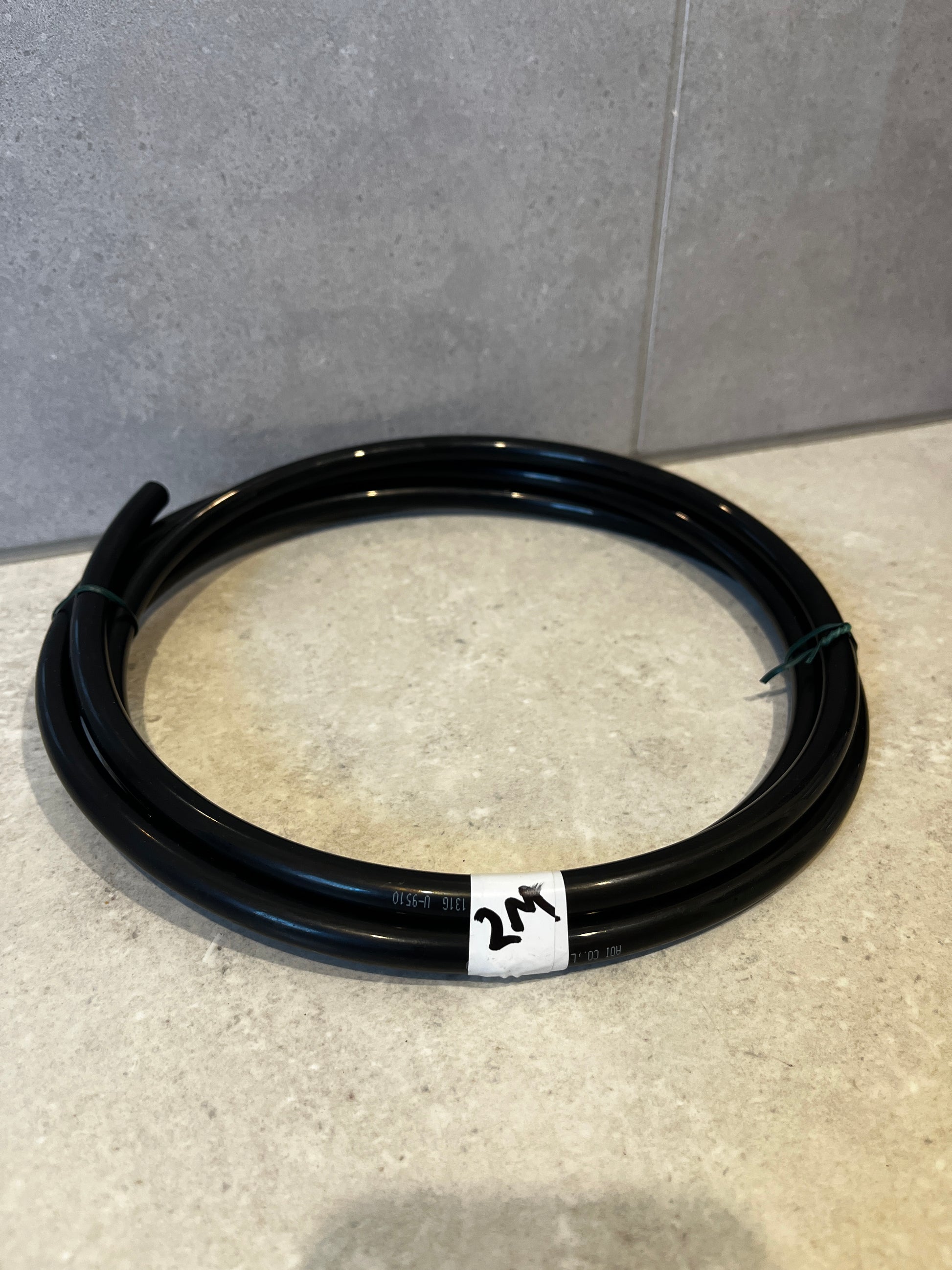 Coiled black flexible tubing with white 2M label on tiled surface