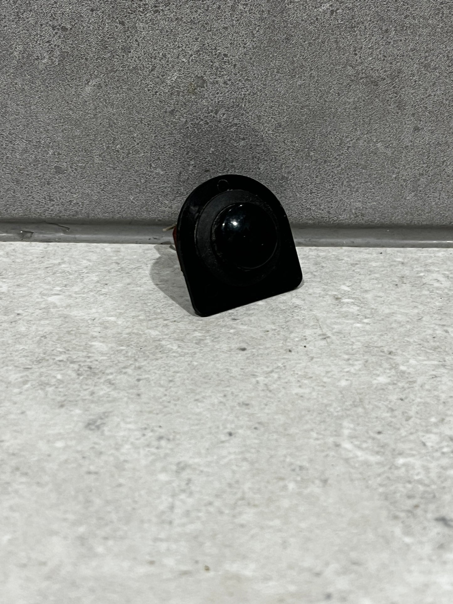 Front view of black round rocker switch on gray surface