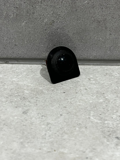 Front view of black round rocker switch on gray surface