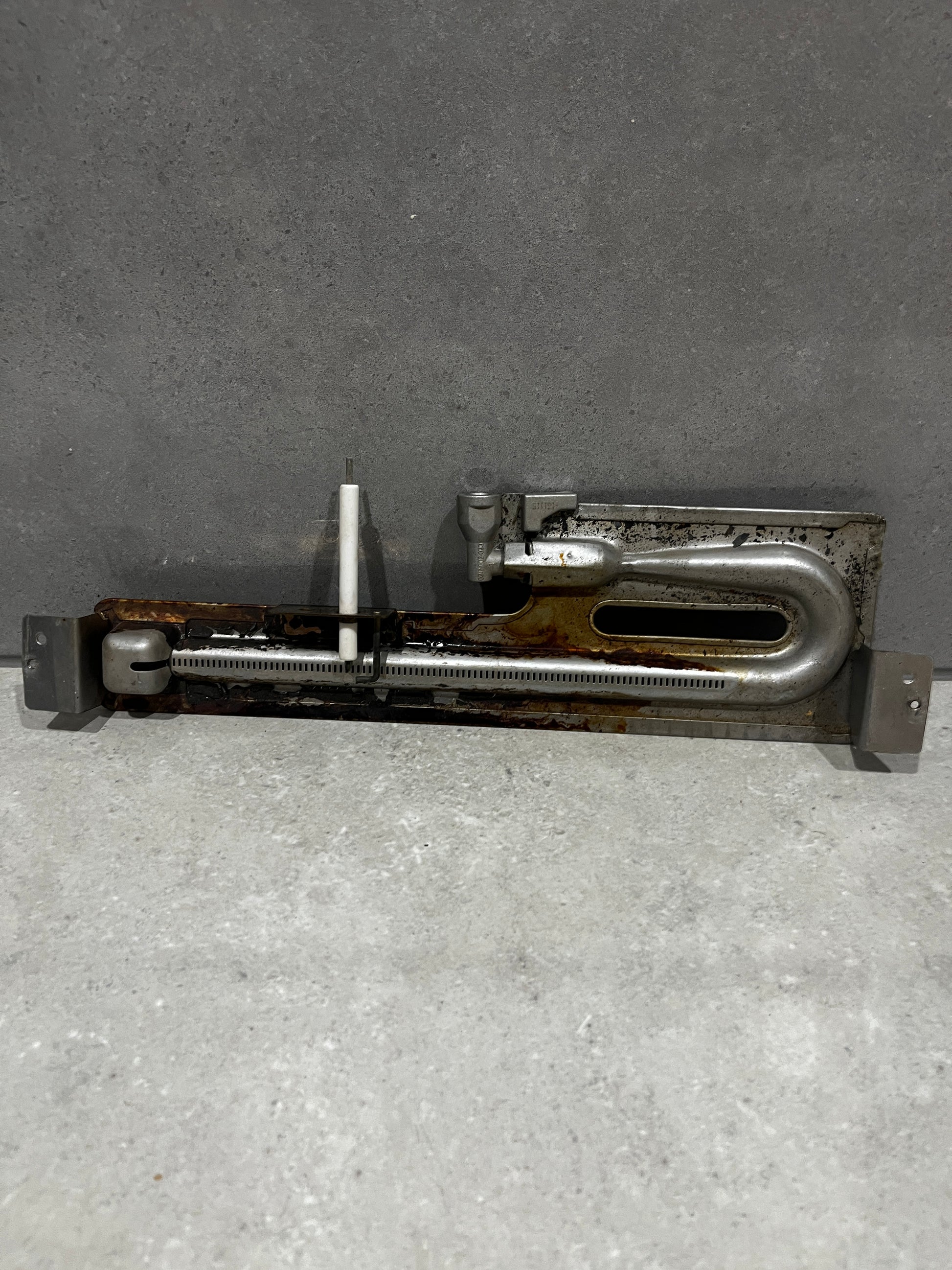 Metal oven burner assembly with attached ceramic ignition electrode and mounting brackets