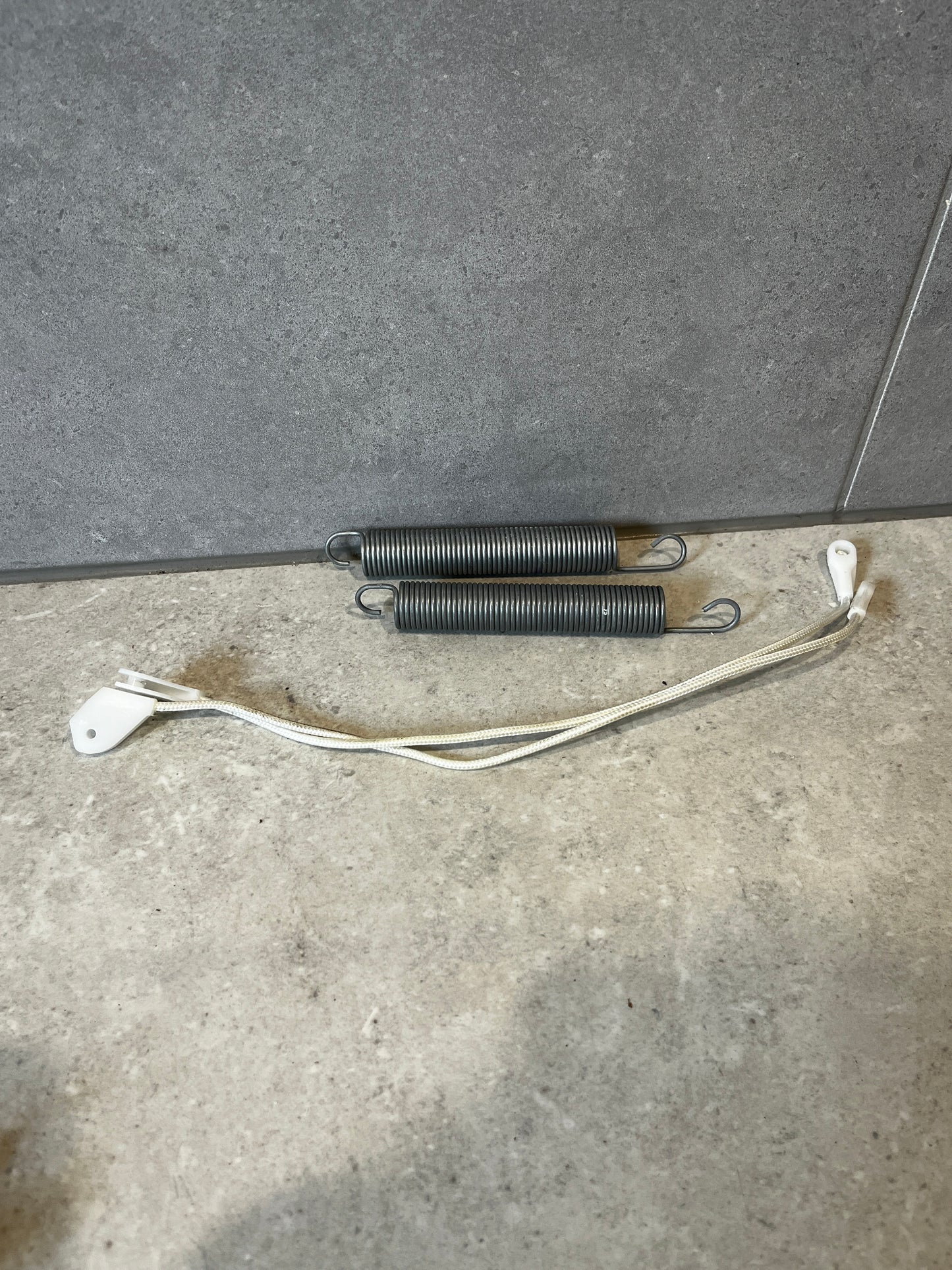 Appliance replacement door springs and braided nylon cable set on gray surface