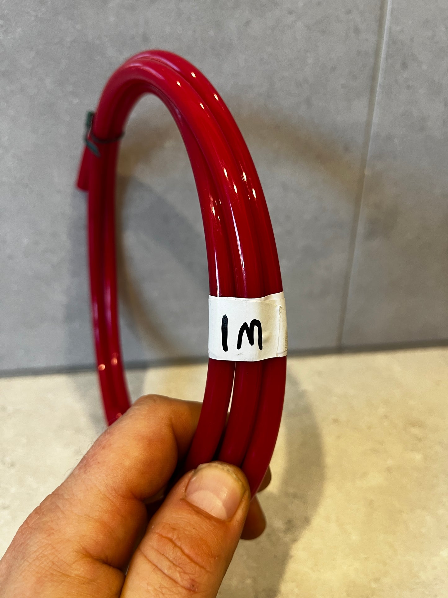 Close-up of hand holding red polyurethane tubing coil labeled 1 meter