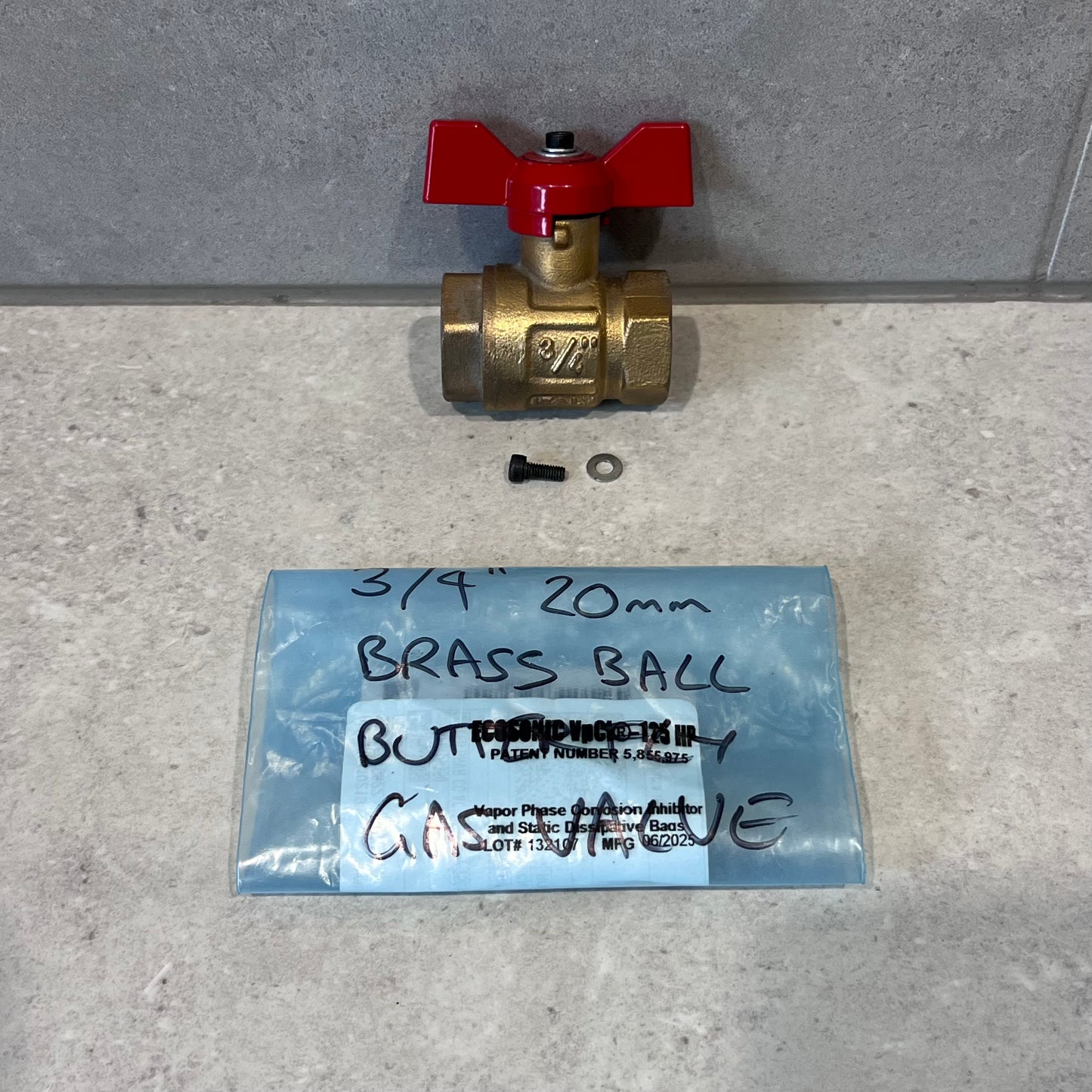 3/4 inch brass ball valve with red butterfly handle, screw, washer, and labeled packaging on gray surface