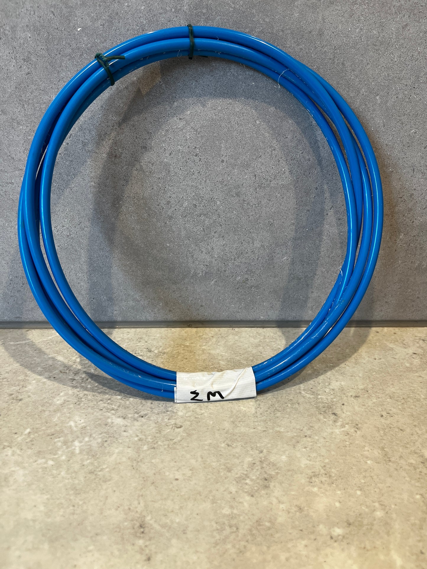 Coiled blue pneumatic tubing on grey surface with white label marking 2 meters