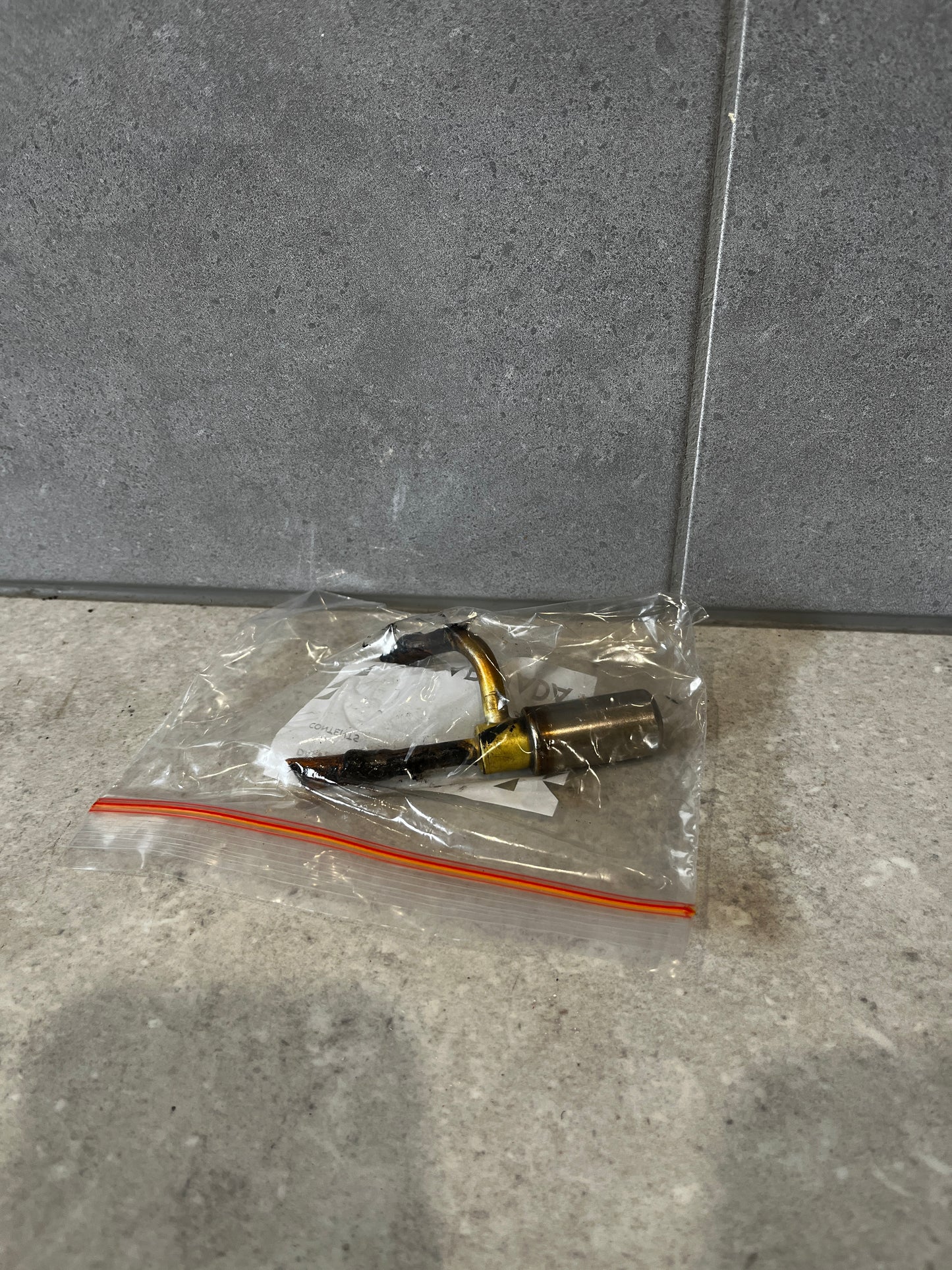 Metal nozzle fitting assembly in a sealed plastic bag on a gray surface