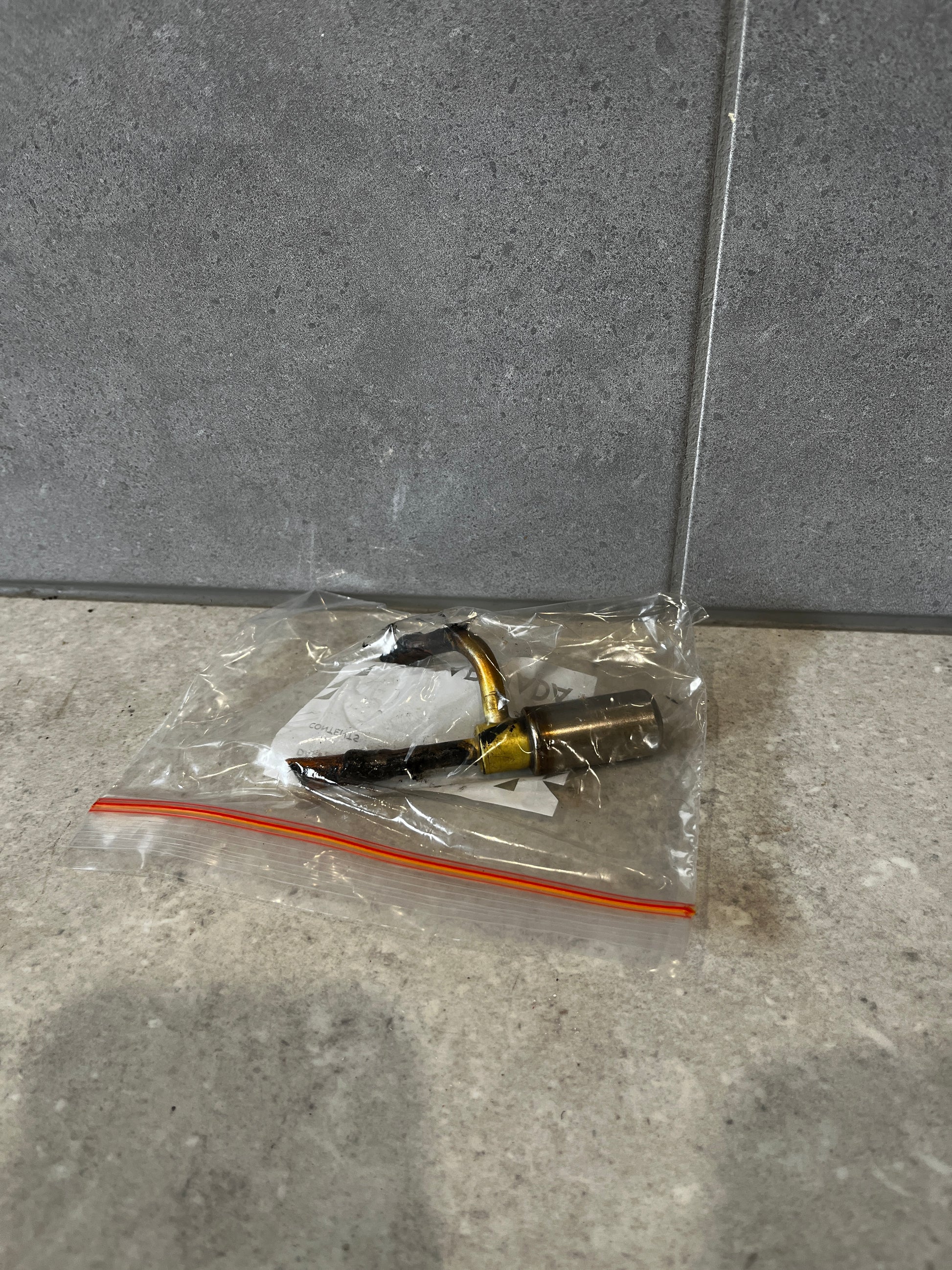 Metal nozzle fitting assembly in a sealed plastic bag on a gray surface