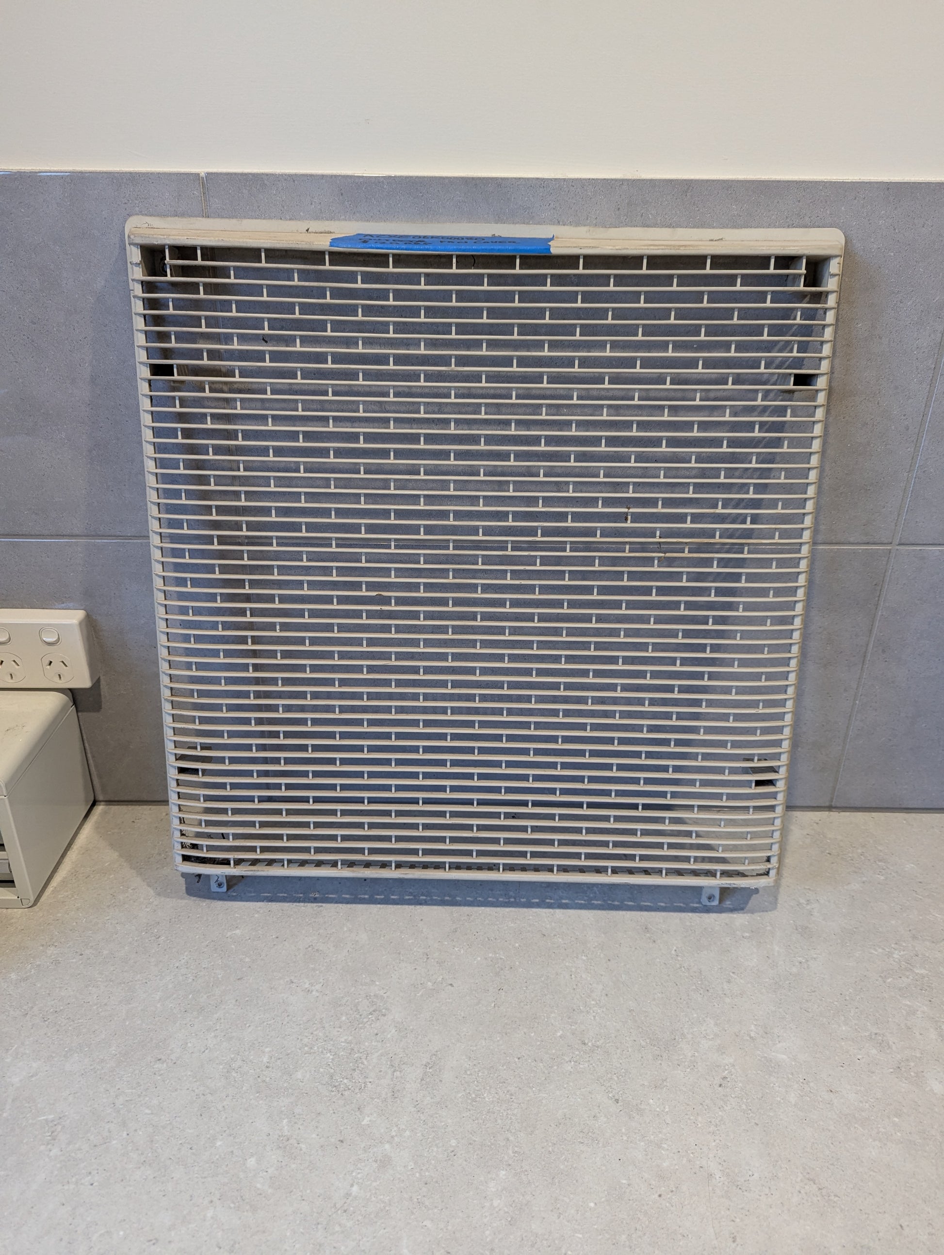 Outdoor fan cover grille standing on floor next to wall socket