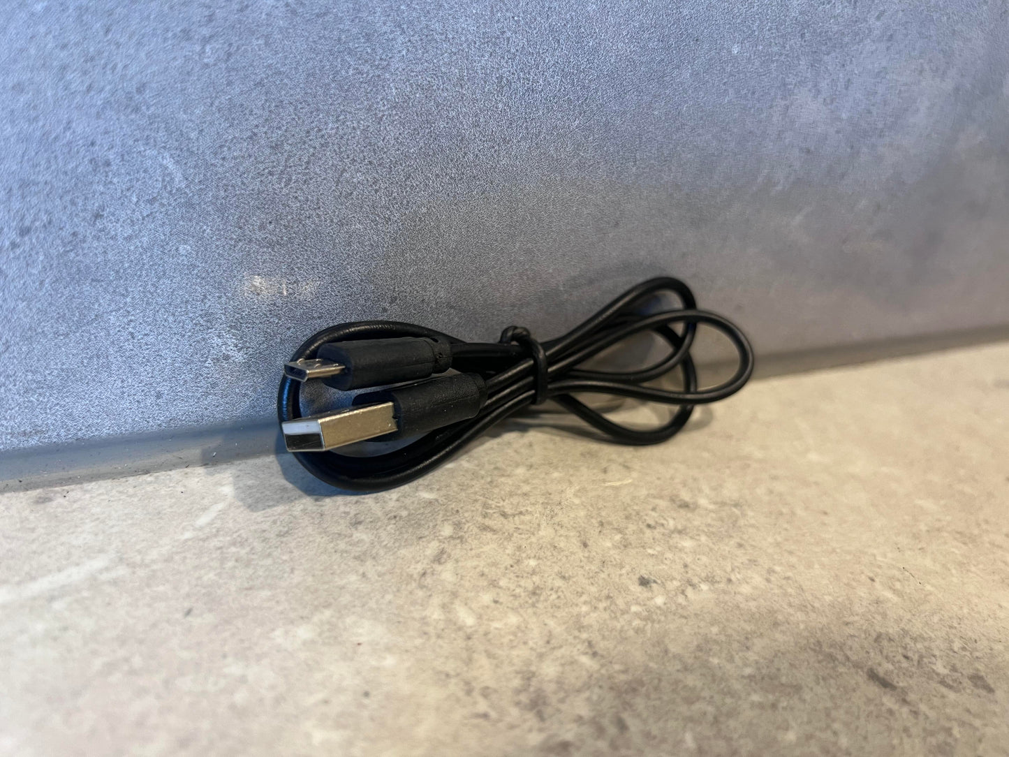 Coiled USB-A to USB-C black charging cable on a stone surface